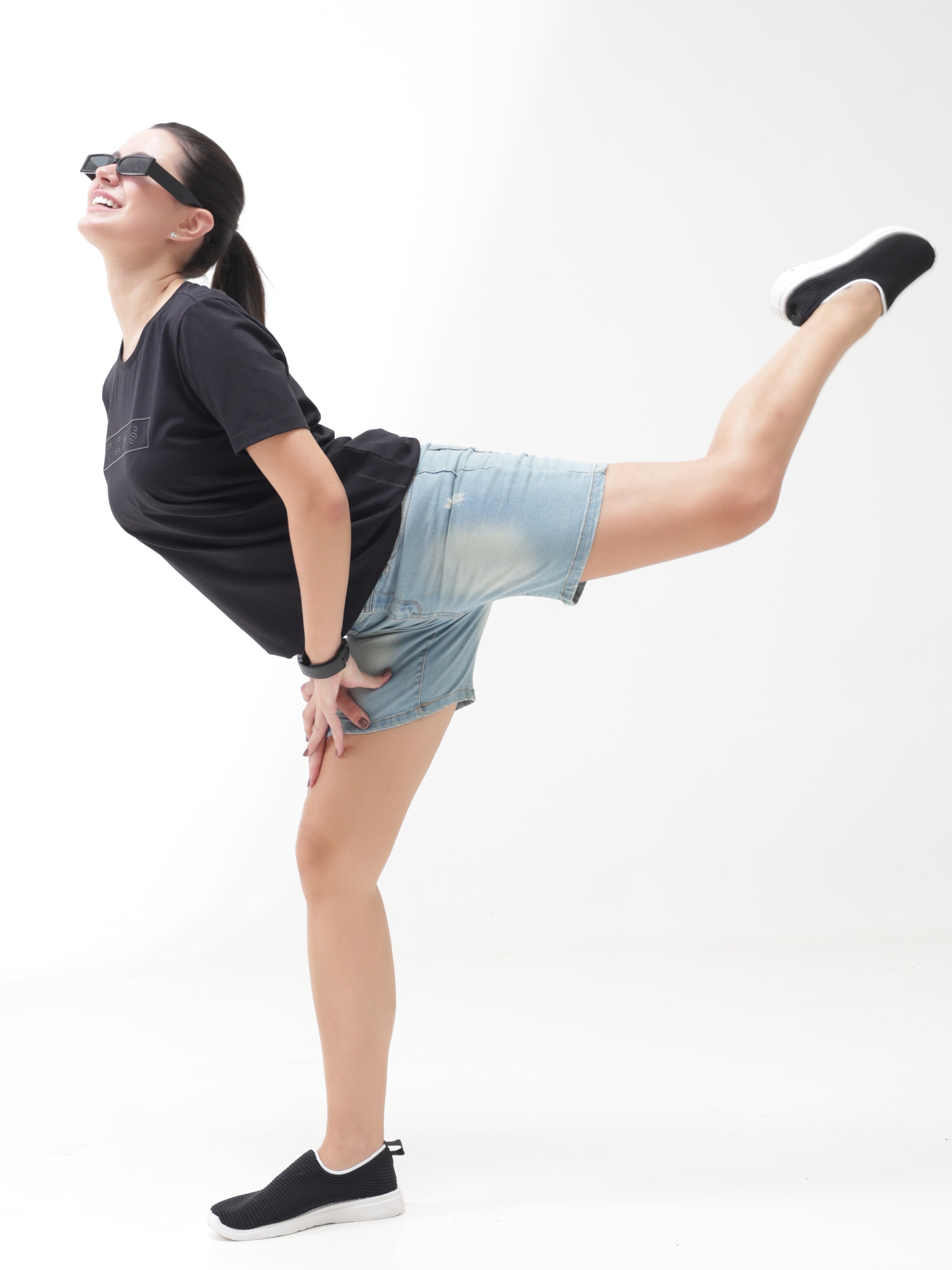 Woman in a Midnight Elegance Turms T-shirt and denim shorts performing a yoga pose, showcasing stain-proof, odor-resistant, and stretchable features.