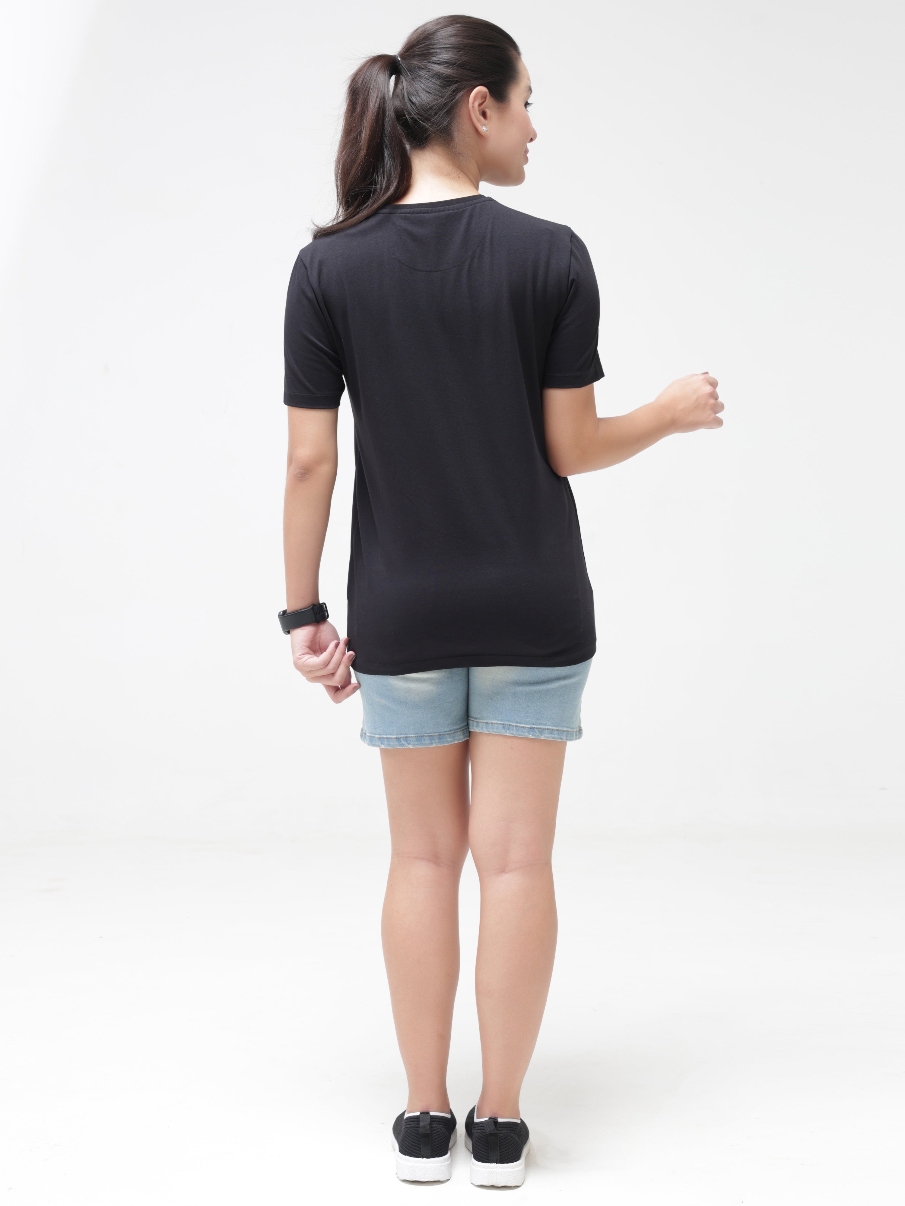 Woman wearing black anti-stain, anti-odour Turms T-shirt with round neck and denim shorts. Stretchable and tailored fit, trending intelligent apparel.