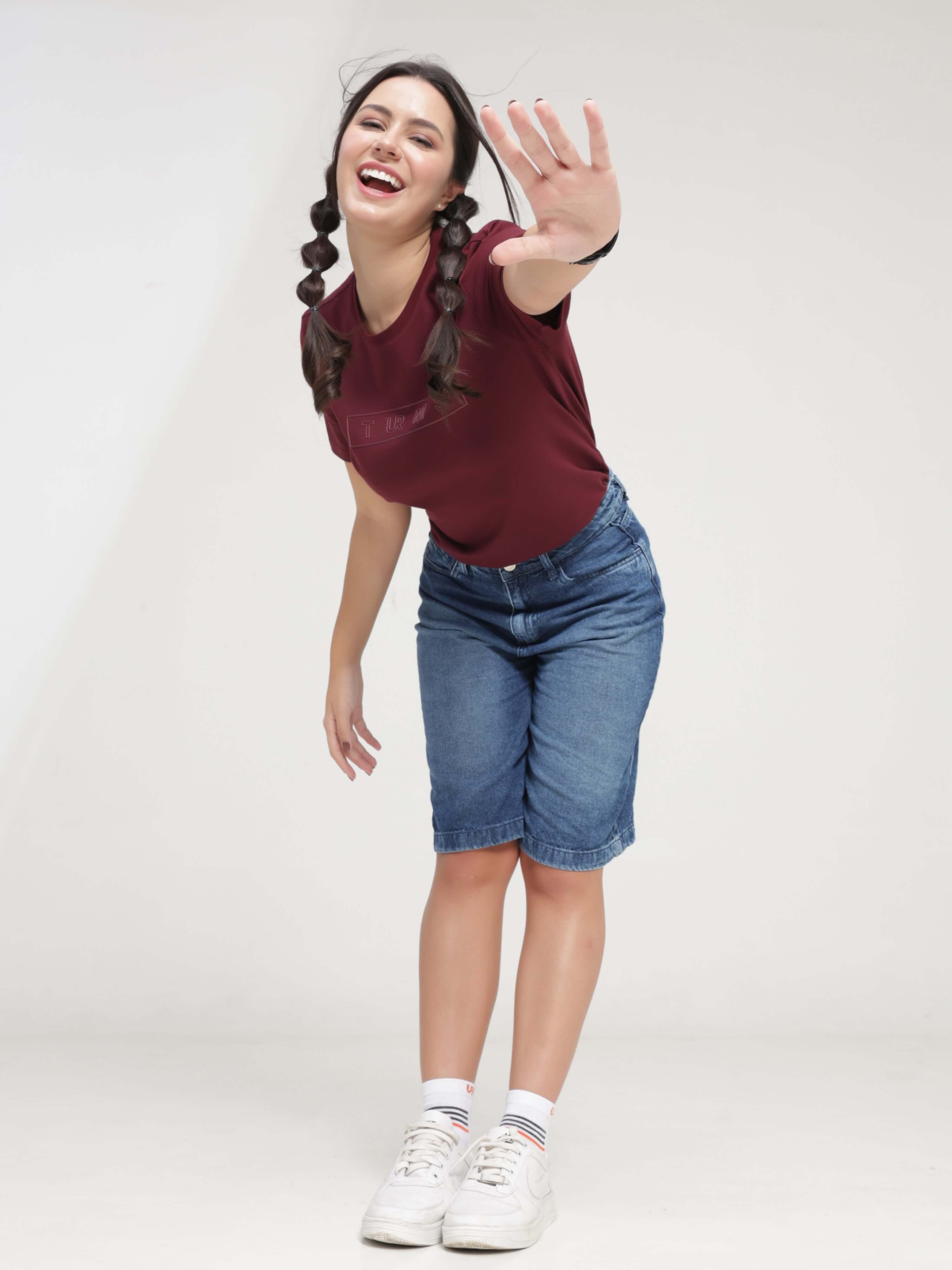 Woman wearing Burgundy Elite round-neck Turms T-shirt and denim shorts, showcasing anti-stain, anti-odor, and stretchable intelligent apparel.