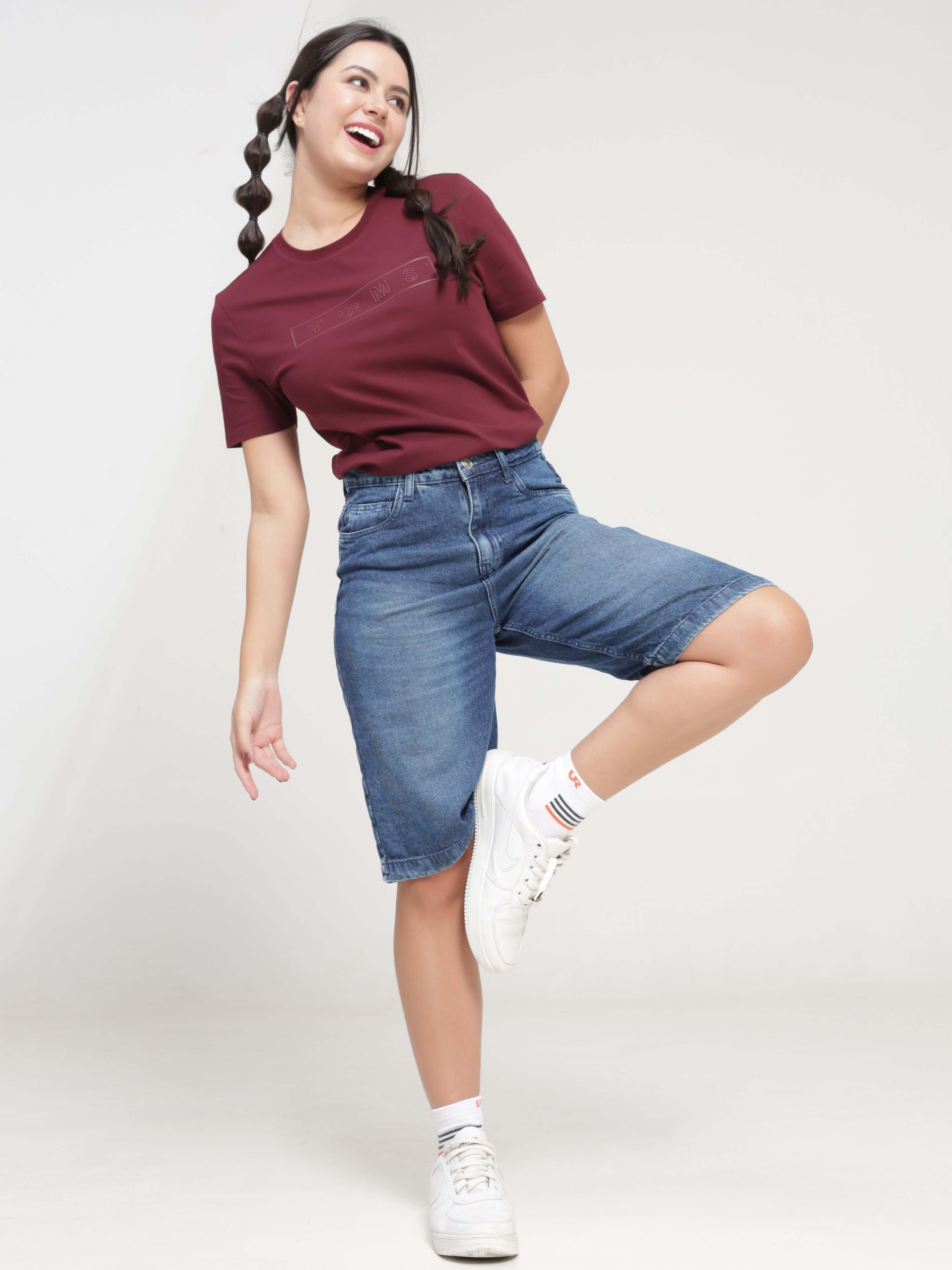 Woman wearing Burgundy Elite anti-stain and anti-odor Turms T-shirt with denim shorts, showcasing the tailored fit and stretchable fabric.