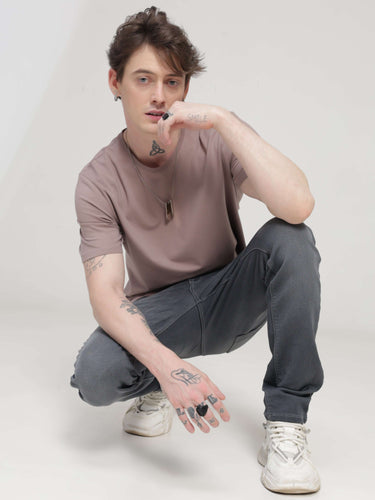 Man wearing Dusky Maroon round-neck Turms T-shirt, stylish and stain-resistant, tailored fit, paired with casual jeans and white sneakers.