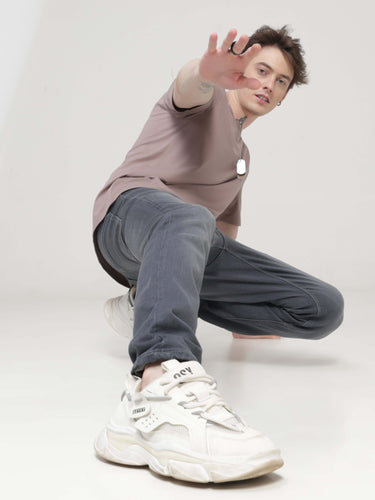 Man wearing Dusky Maroon round neck t-shirt and grey pants in a dynamic pose, showcasing stylish and stain-proof apparel for men.
