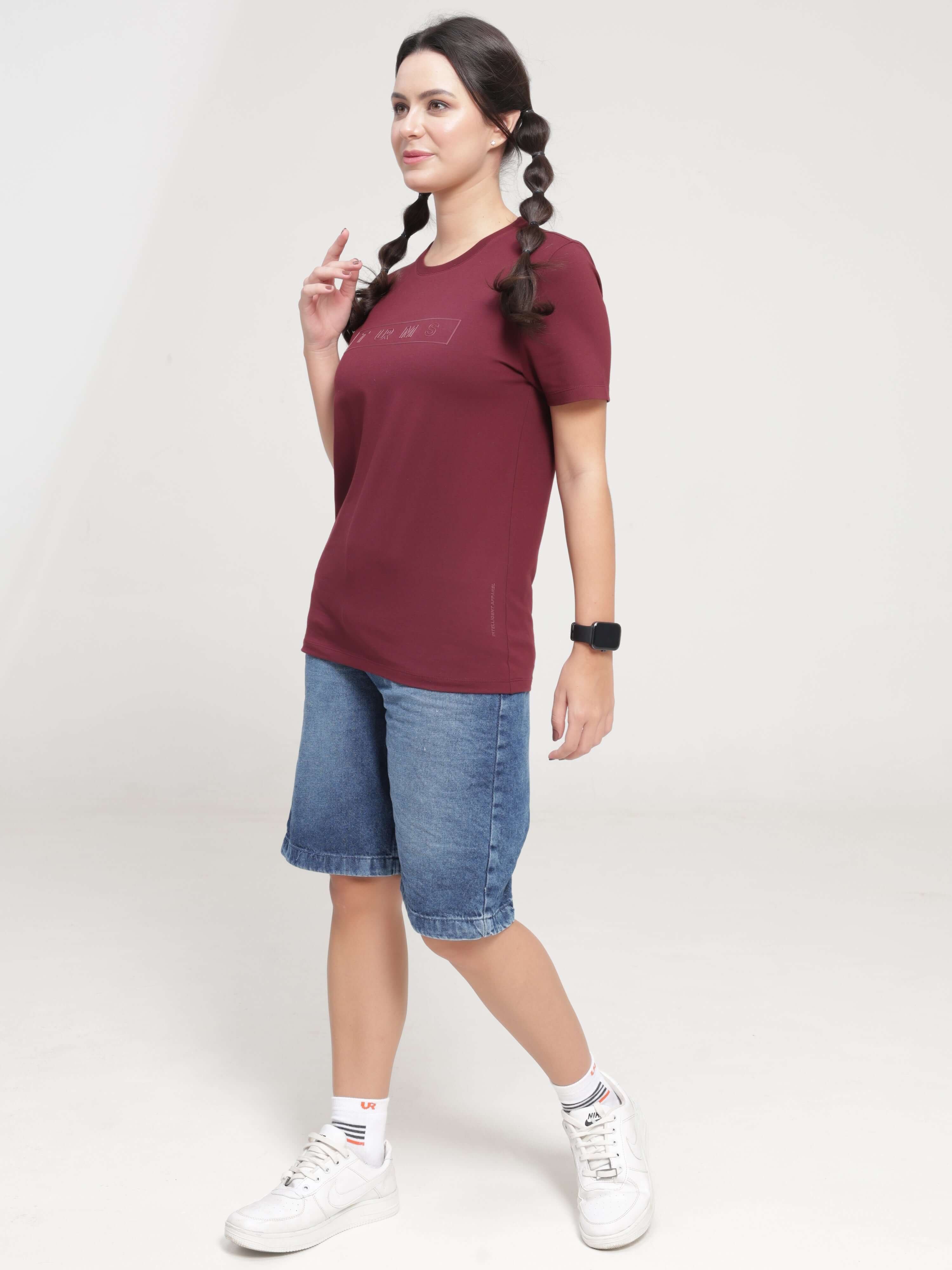 Woman in Burgundy Elite anti-stain, anti-odor Turms T-shirt with tailored fit, round neck, and stretchable fabric, paired with denim shorts.