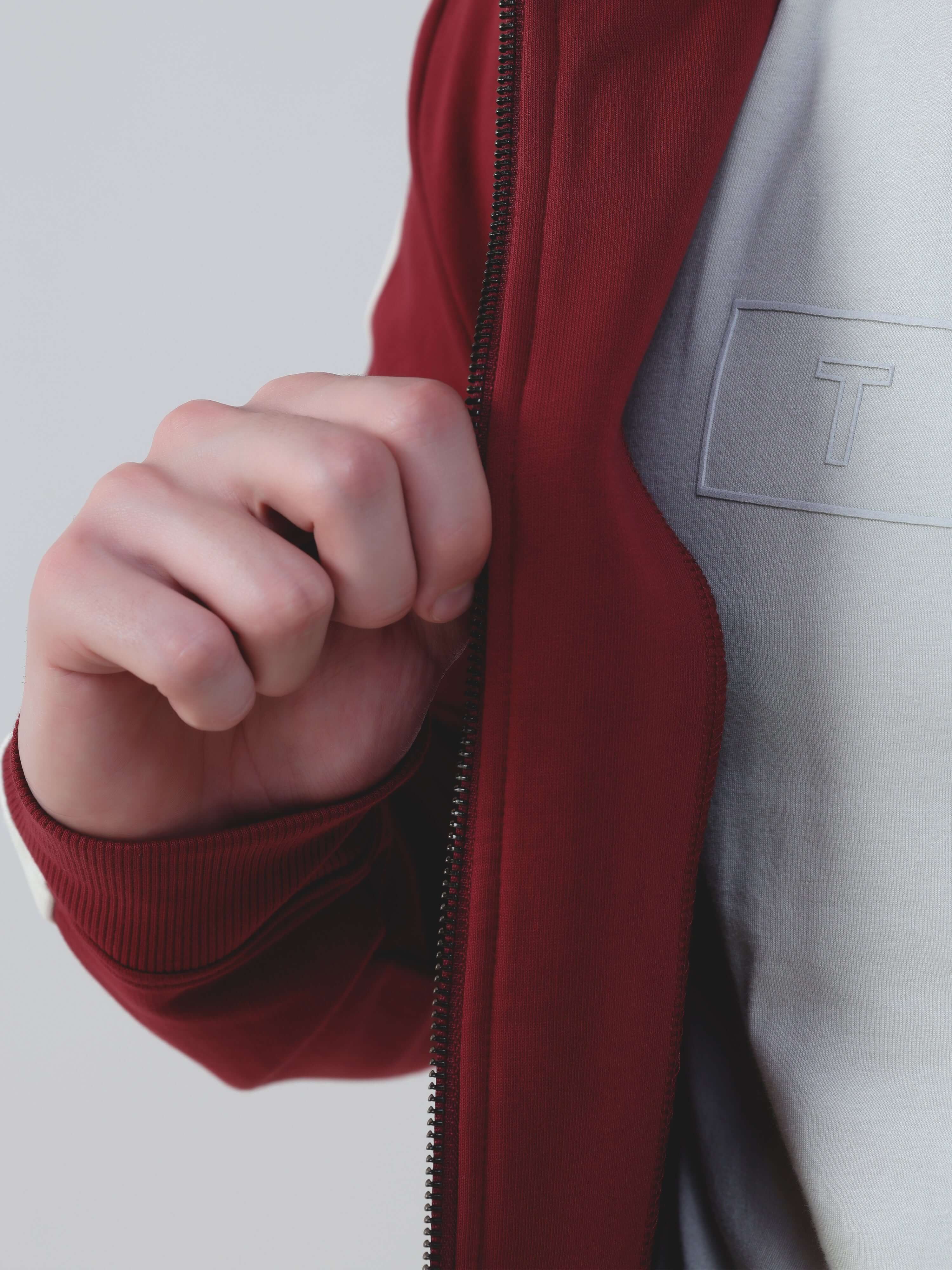 Close-up of a hand holding a zipper on a burgundy jacket from the Turms Intelligent co ord set.