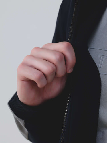 Close-up of hand unzipping Turms Intelligent Cord Set jacket, showcasing sporty design and premium fabric.