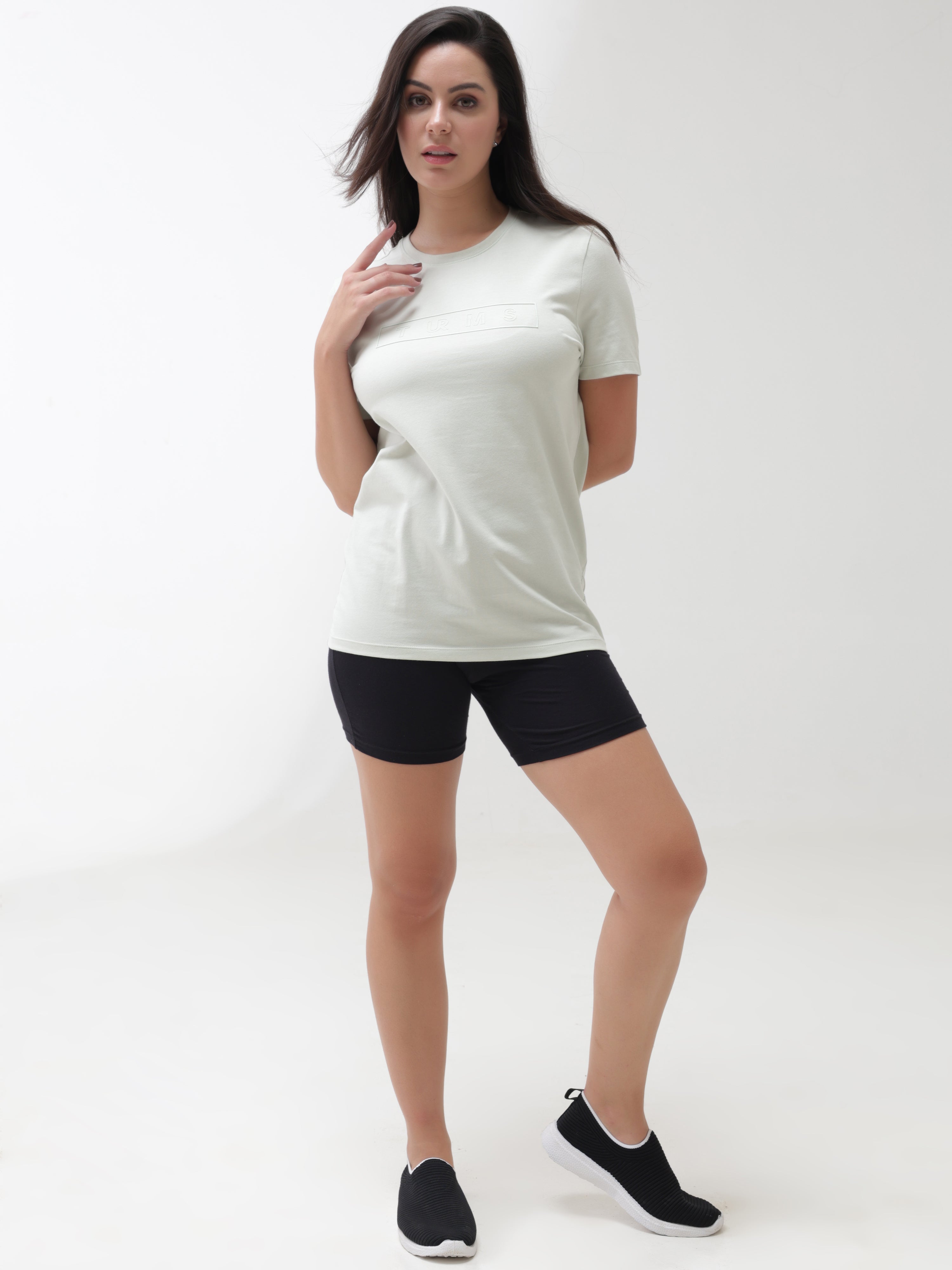 Woman wearing Lime Enigma Turms T-shirt with tailored fit and round neckline, showcasing anti-stain and anti-odor features, paired with black shorts.