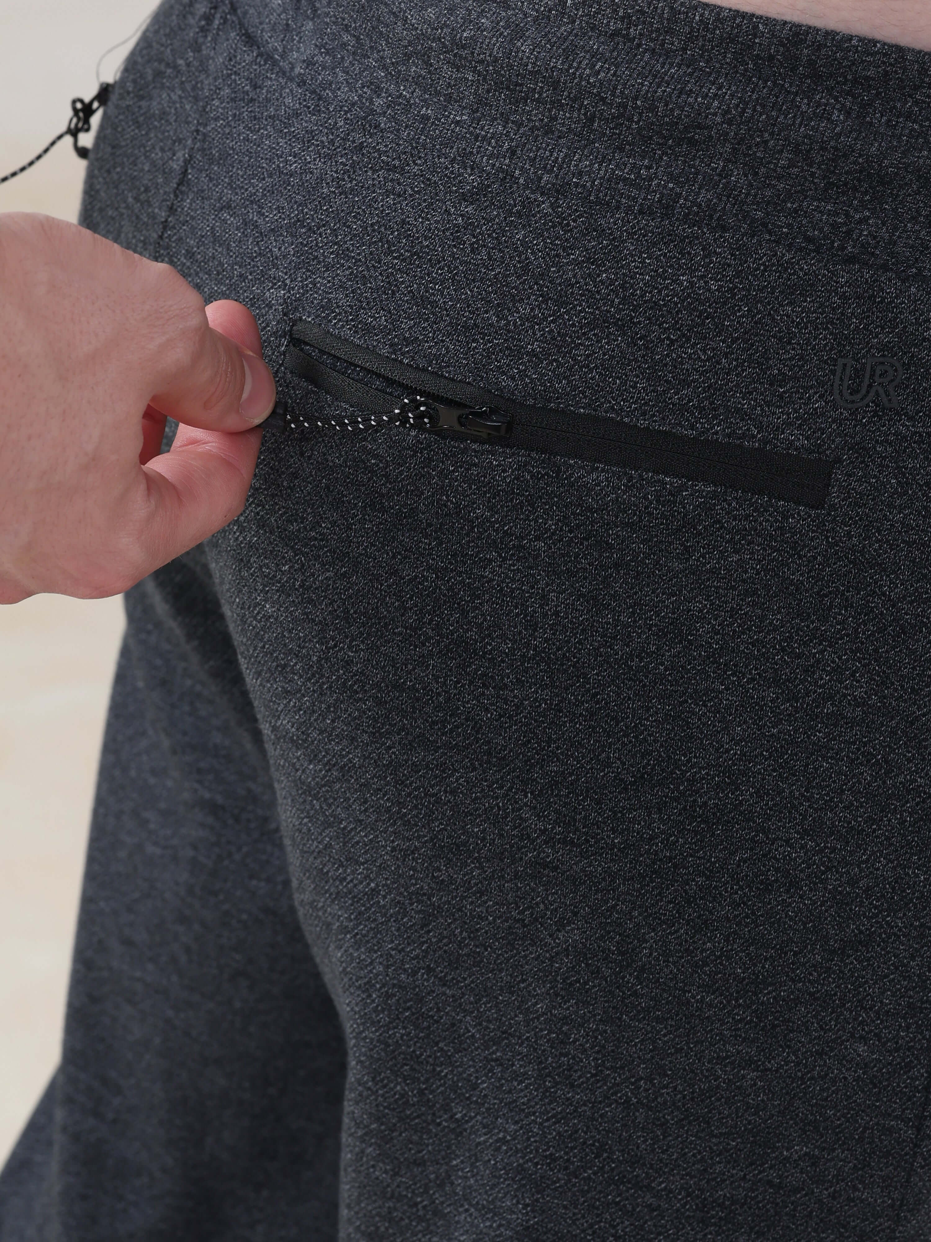 Close-up of a hand using the zipper pocket of navy Turms Intelligent Jogger, featuring waterproof and anti-odour fabric.