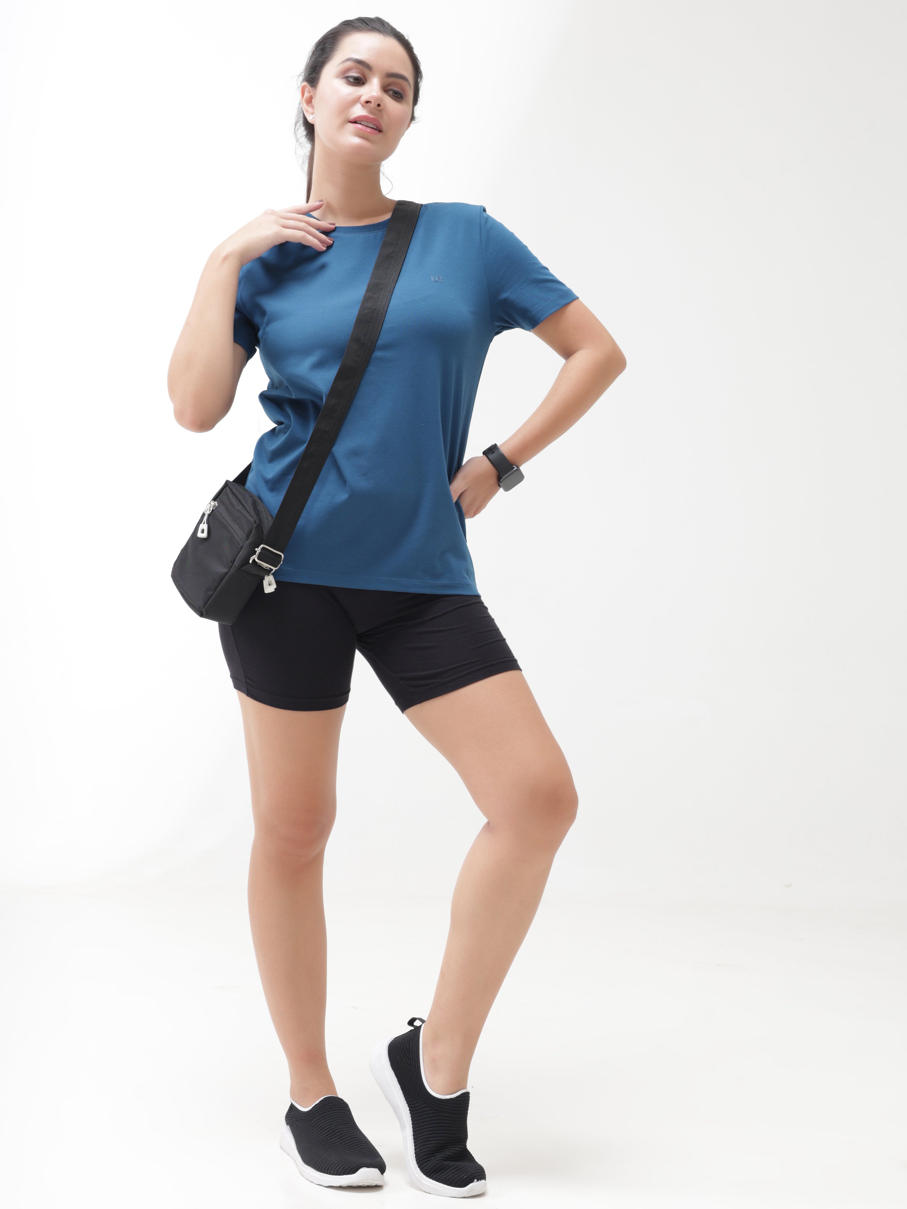 Woman in a Sea Blue Turms anti-stain, anti-odour, and stretchable round-neck T-shirt, wearing black shorts and a crossbody bag.