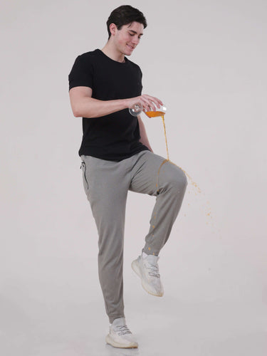 Man in grey joggers demonstrating anti-stain feature by spilling juice, showcasing comfort and style in activewear.
