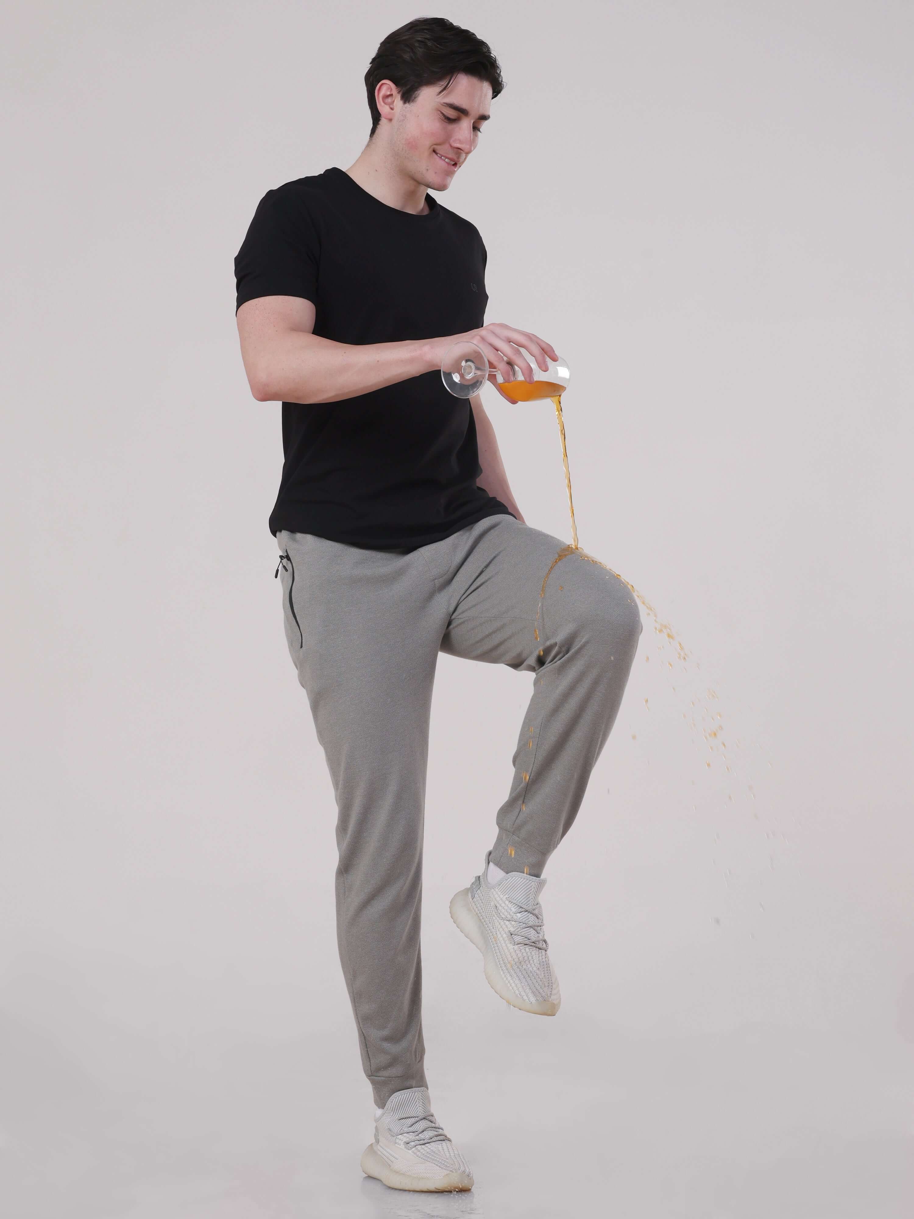 Man in grey joggers demonstrating anti-stain feature by spilling juice, showcasing comfort and style in activewear.