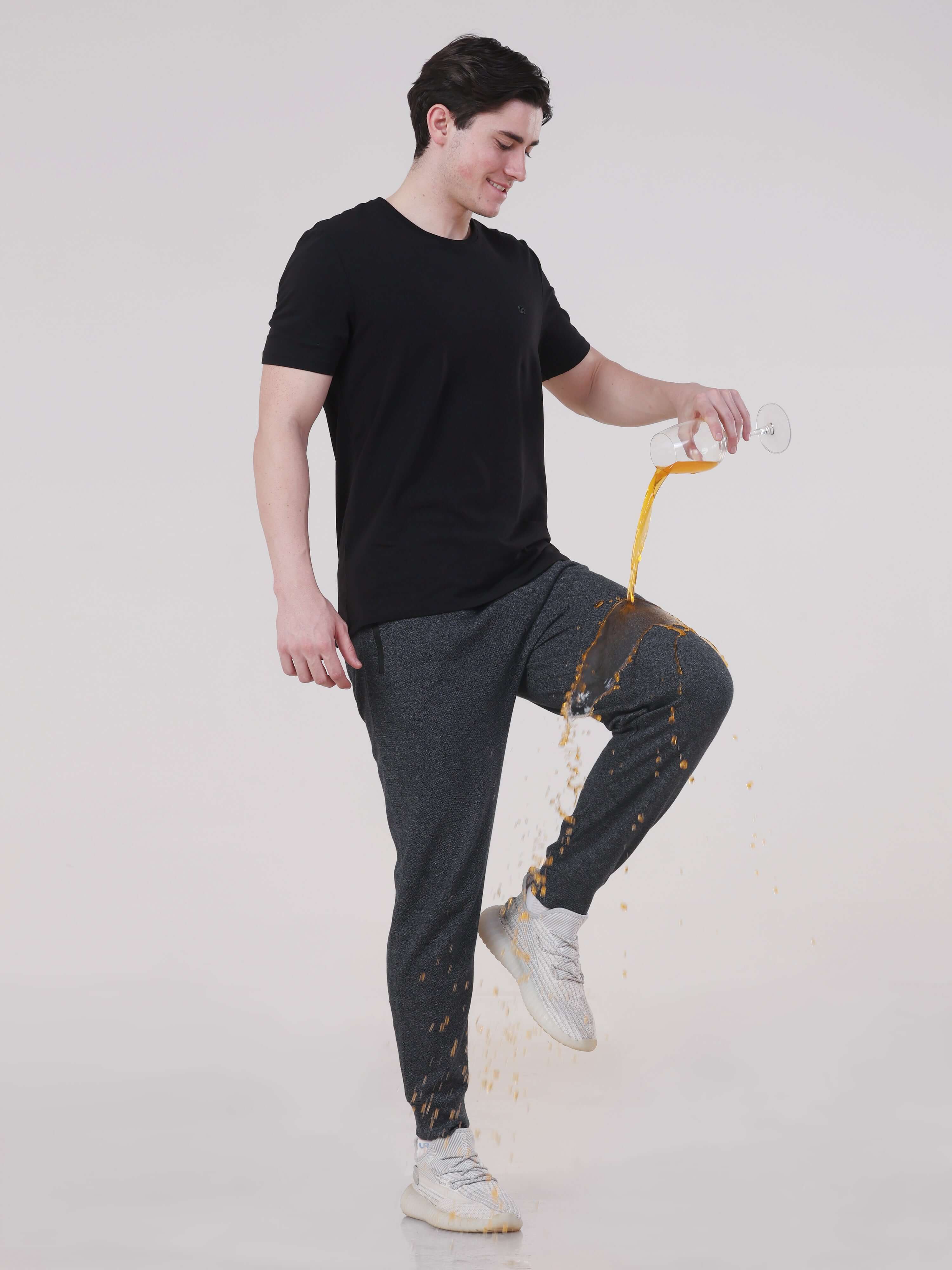 Man in Turms navy joggers pouring liquid, showcasing anti-stain and waterproof features for active travelers.