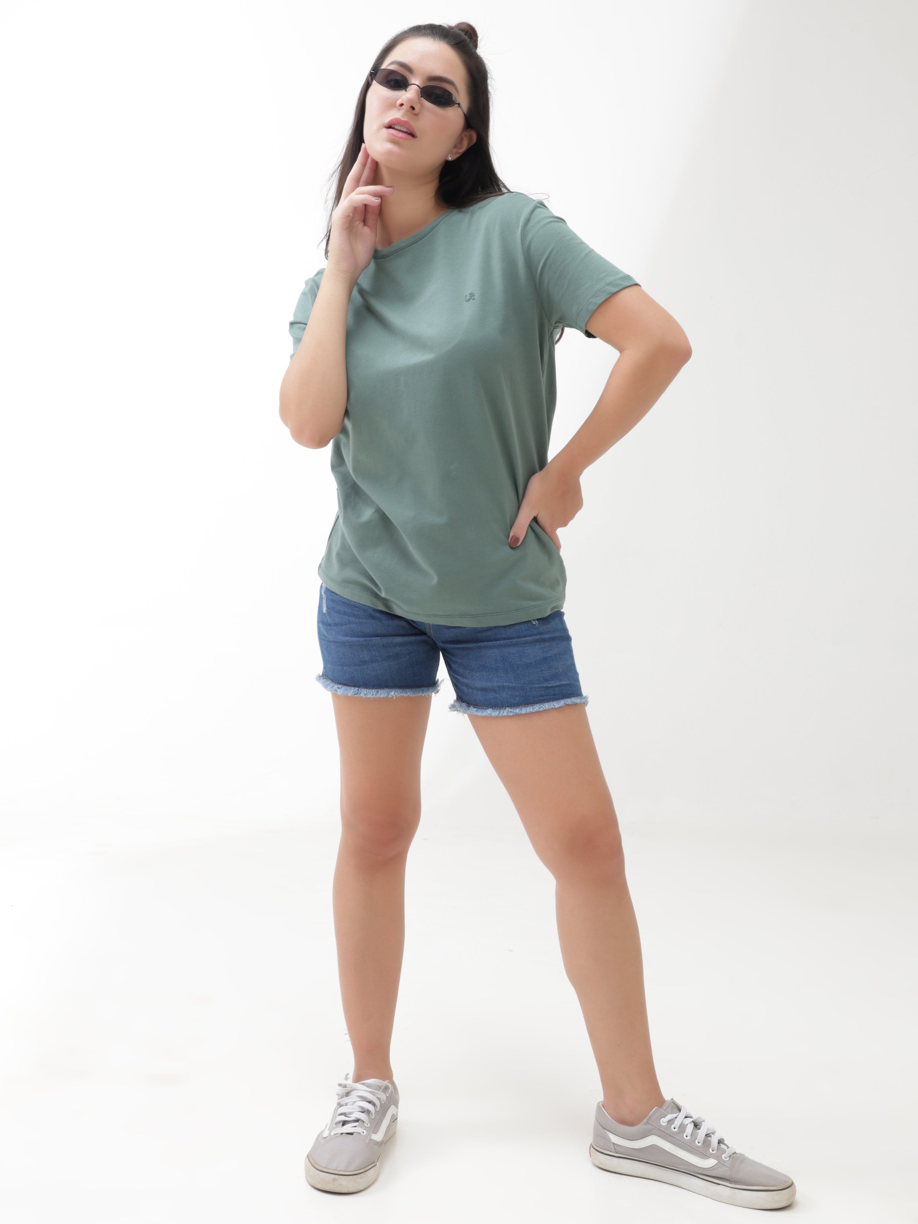 Woman wearing a simple green round neck t-shirt paired with denim shorts and casual sneakers