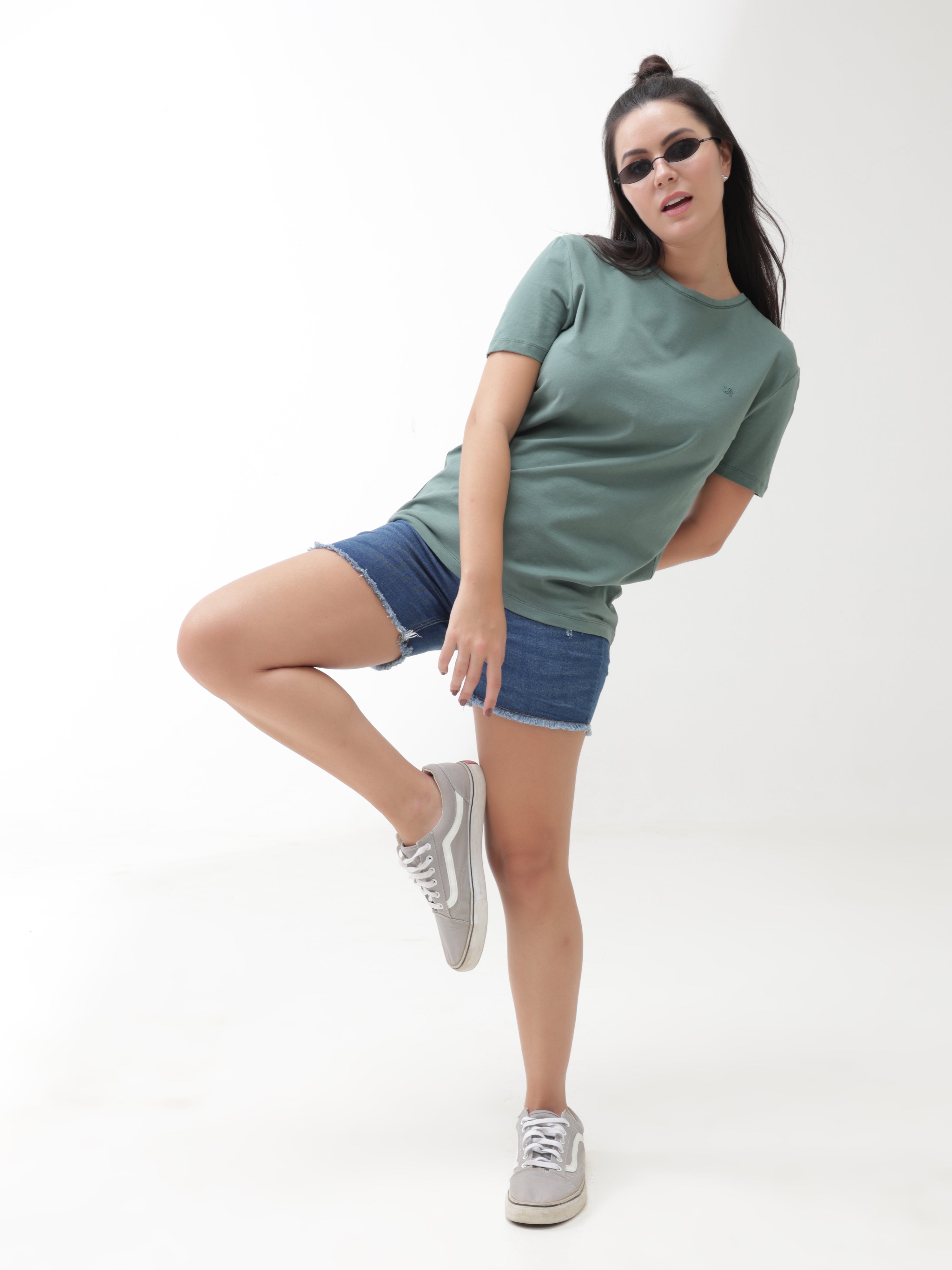 Woman in green Simple Green round-neck t-shirt and denim shorts posing stylishly against a white background