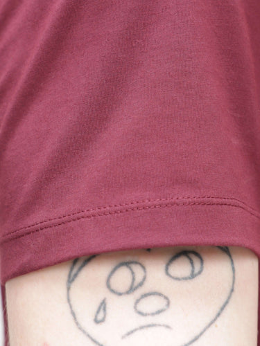 Close-up of Burgundy Elite Turms T-shirt sleeve showing anti-stain fabric and round-neck design over a tattooed arm.