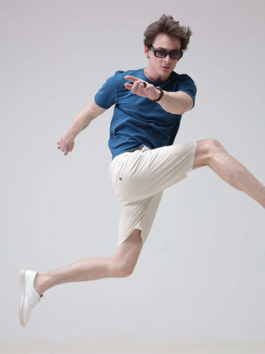 Man wearing Sea Blue round neck t-shirt and white shorts mid-air jump, showcasing stylish and best branded t-shirt for men.