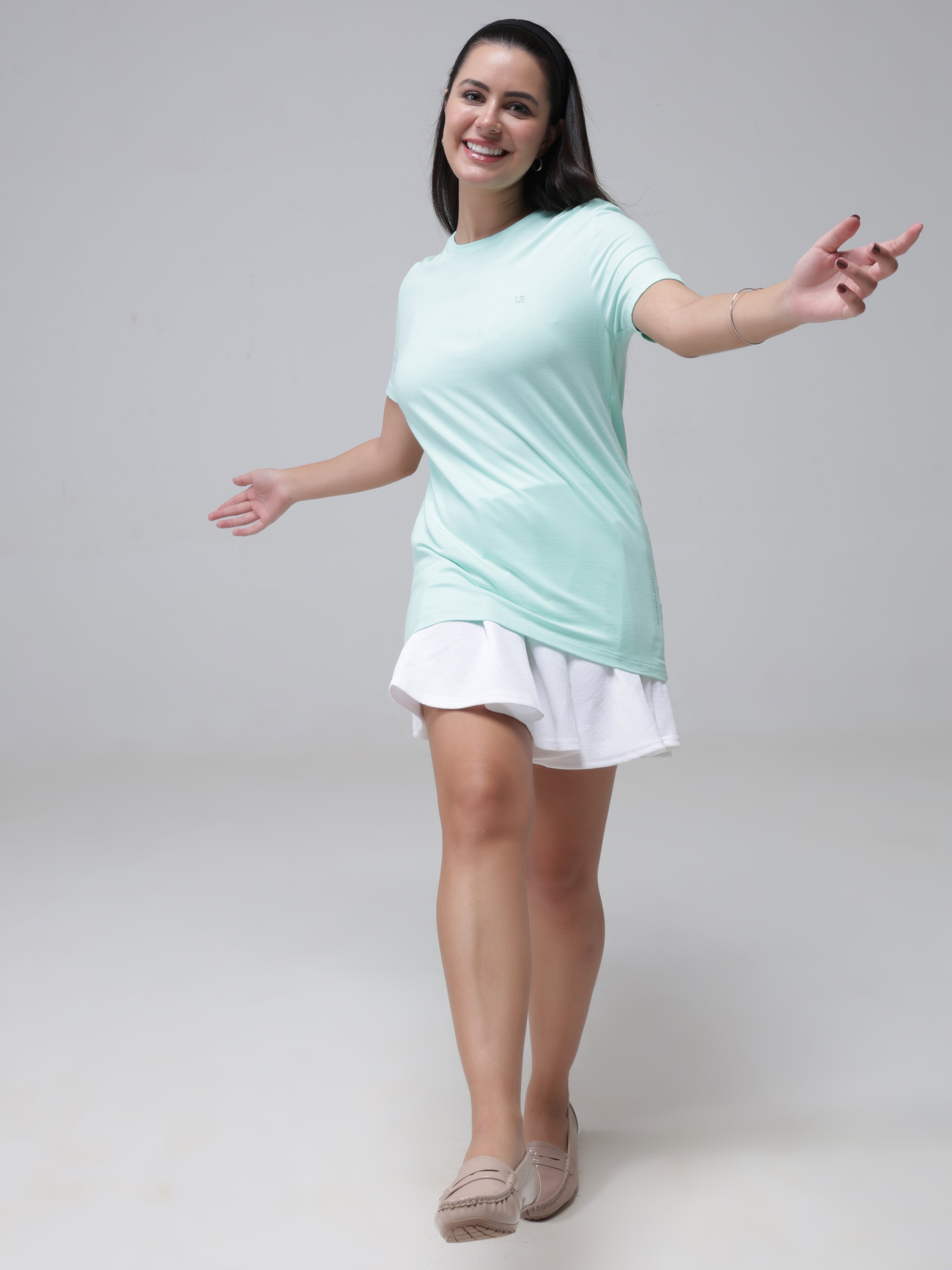 Woman wearing a light green round-neck T-shirt with white skirt, smiling and posing in a casual outfit.