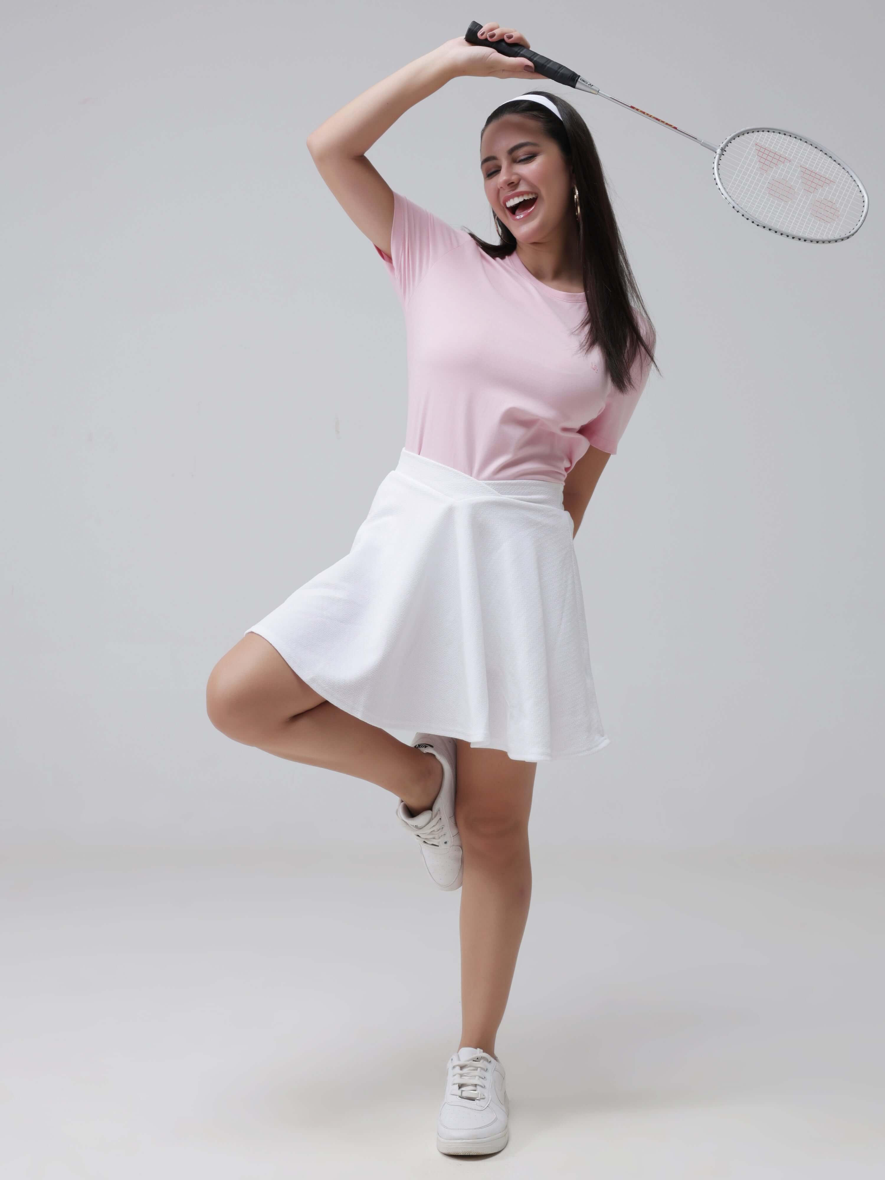 Woman wearing pink round-neck Turms T-shirt and white skirt, holding badminton racket, showcasing anti-stain, anti-odor, stretchable intelligent apparel.