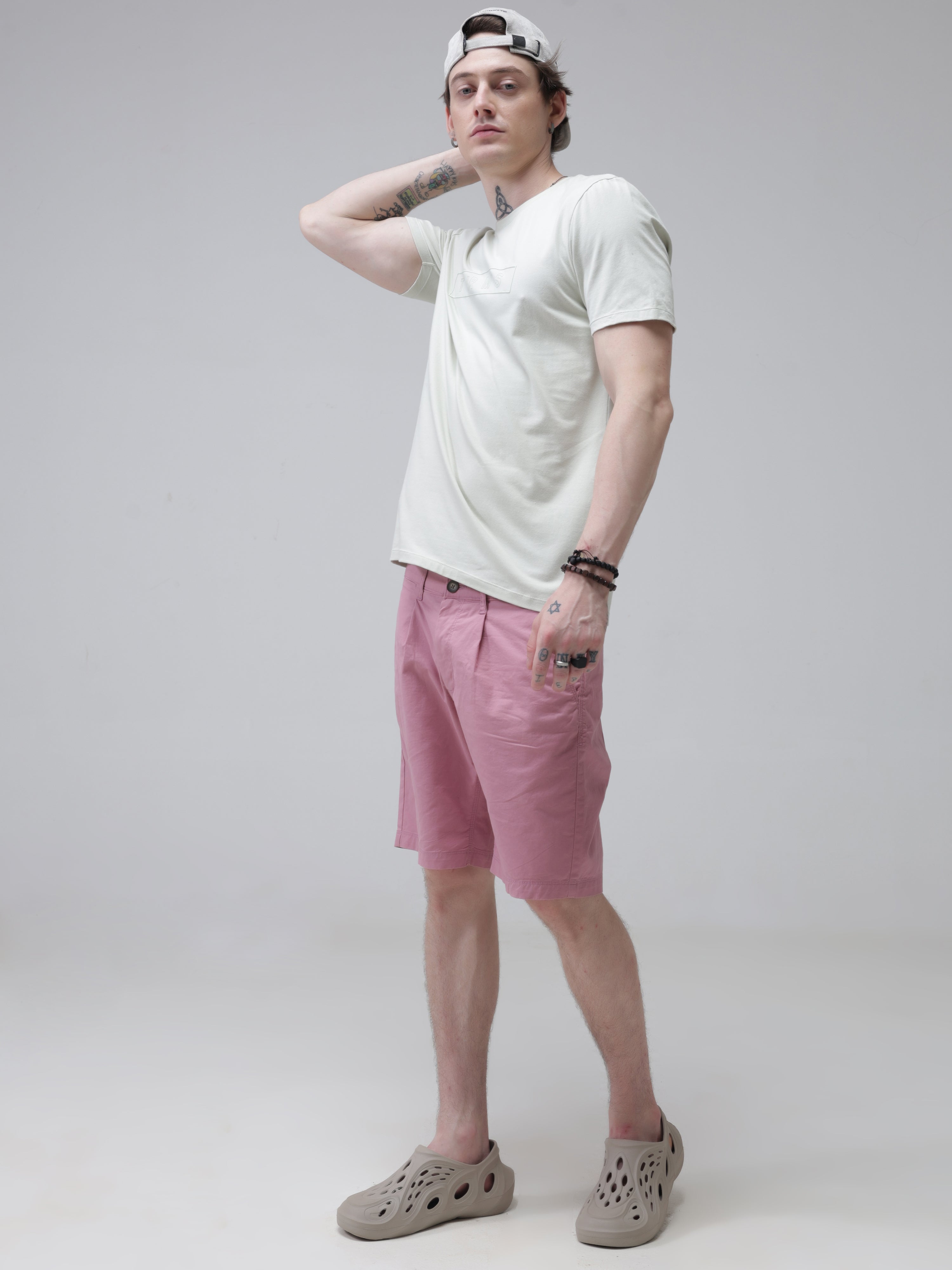 Man wearing a white round-neck Turms T-shirt and pink shorts with beige shoes, striking a pose