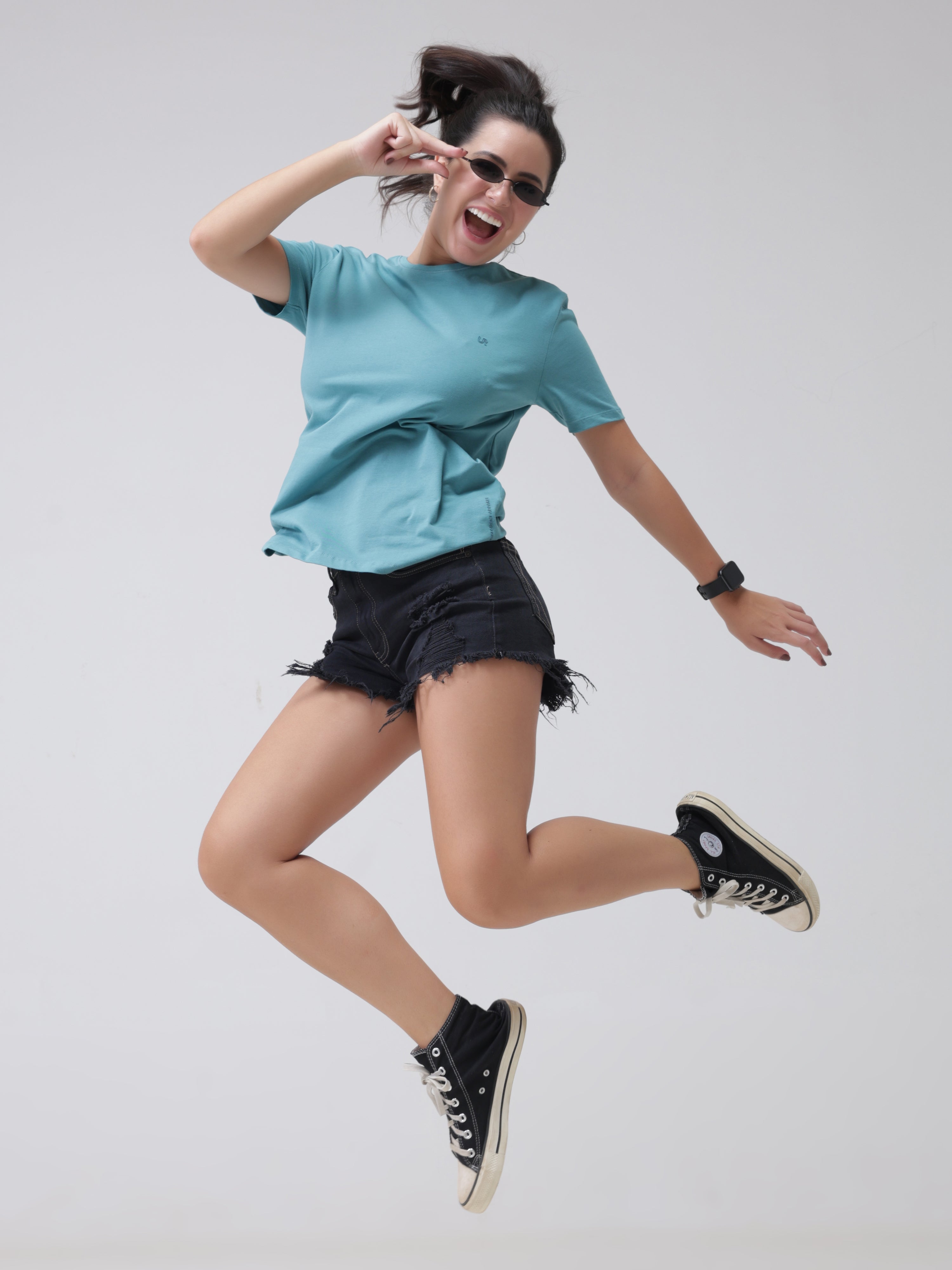 Woman wearing a blue round-neck T-shirt and black shorts, jumping joyfully in stylish casual attire.