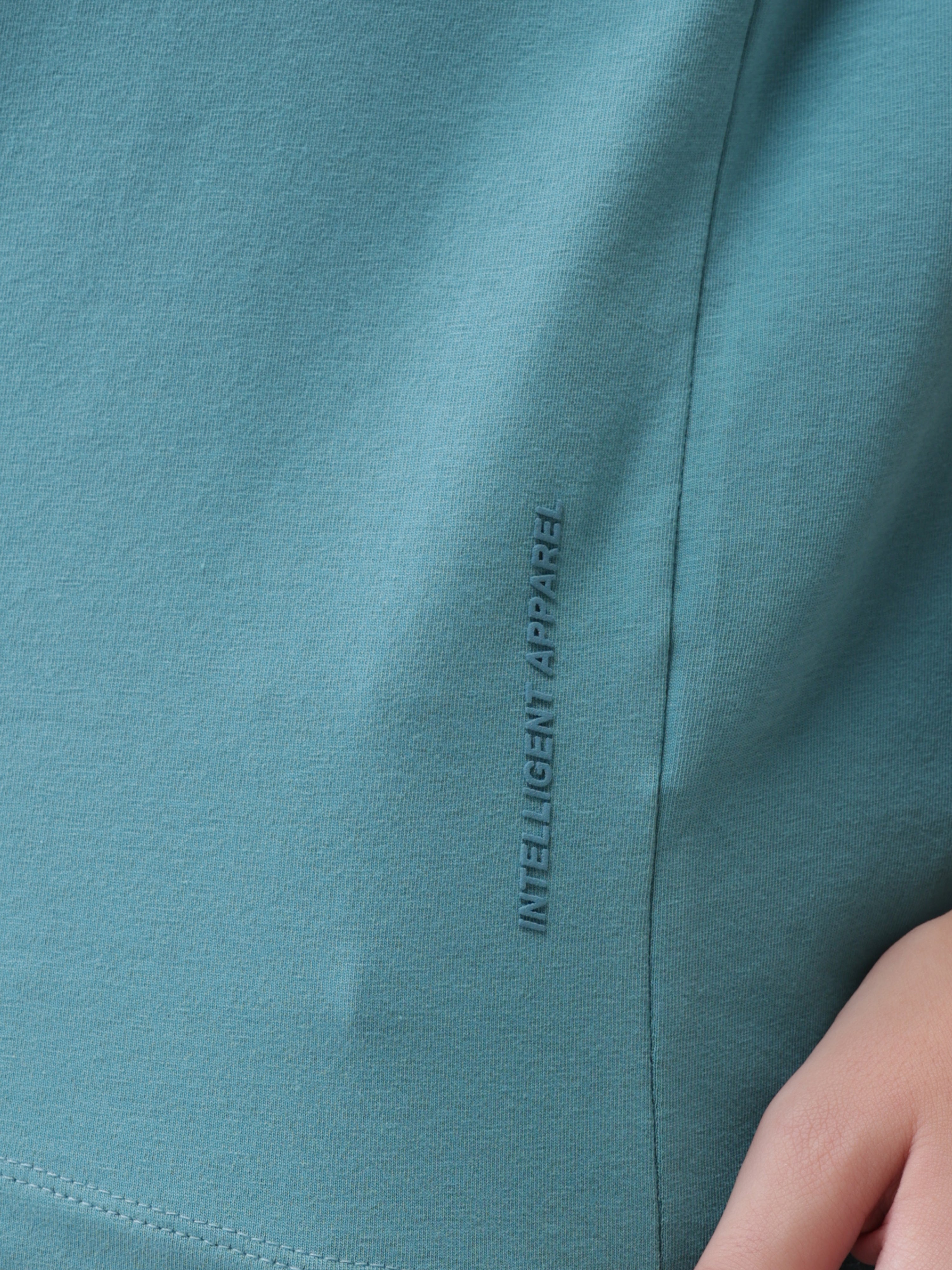Close-up of turquoise Turms T-shirt, displaying "Intelligent Apparel" text on fabric.