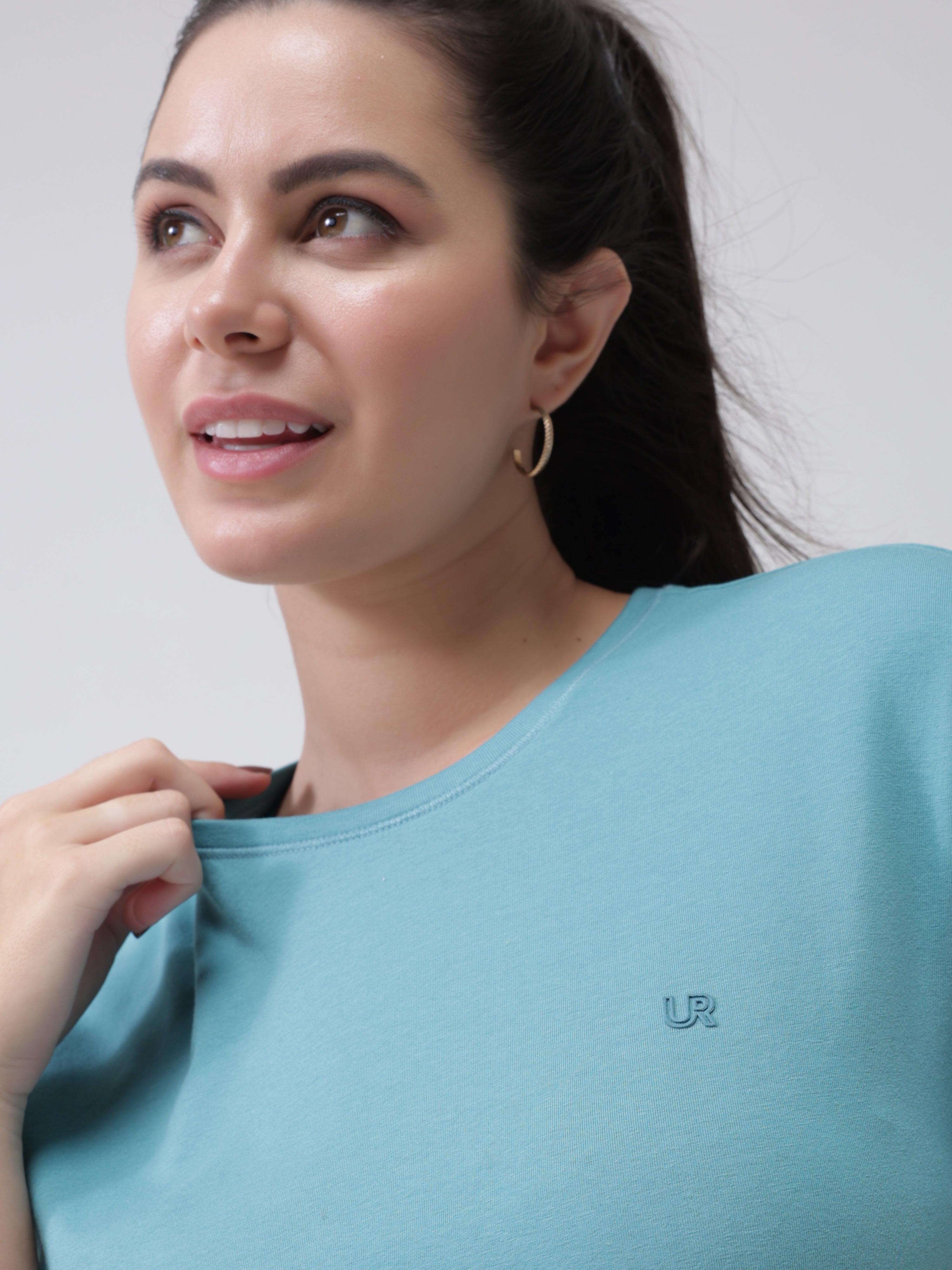 Woman wearing a turquoise round-neck Turms T-shirt with a small logo on the chest, showcasing stylish and comfortable casualwear.