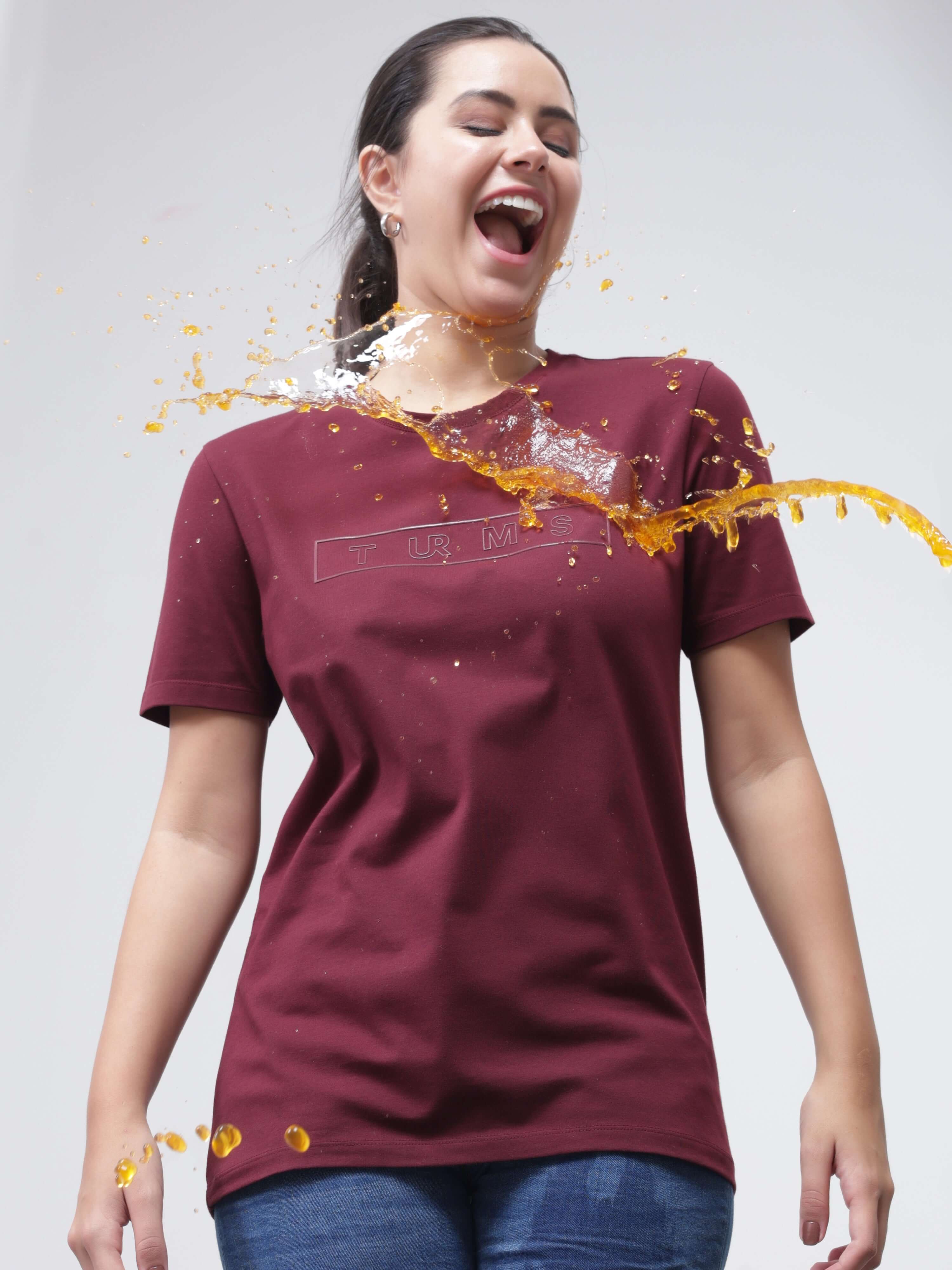 Woman wearing Burgundy Elite Turms T-shirt with spill deflecting off, showcasing anti-stain and anti-odour capabilities.