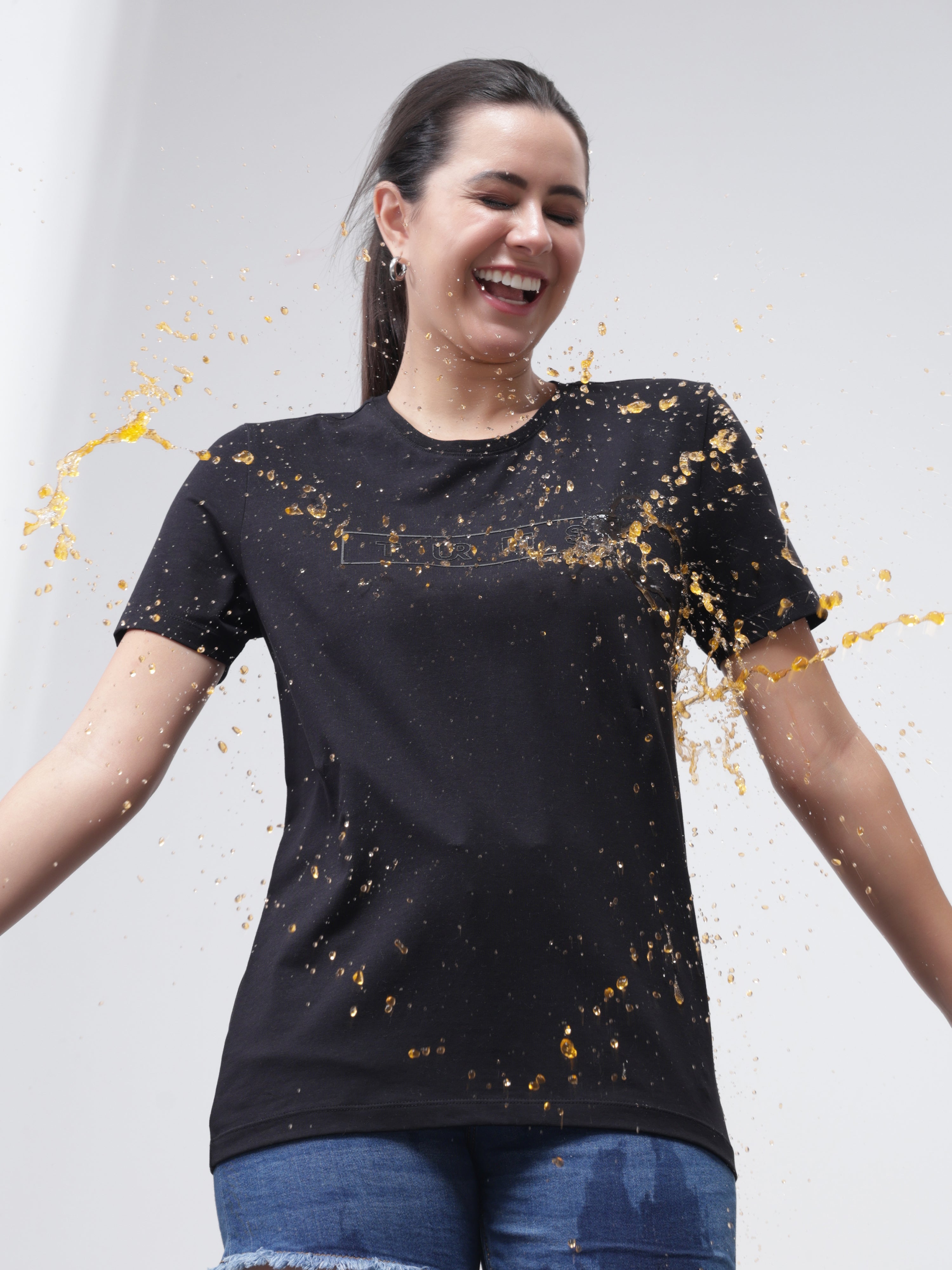 Woman wearing Turms Midnight Elegance T-shirt demonstrating anti-stain and anti-odor properties with liquid spill, showcasing stain-proof technology.