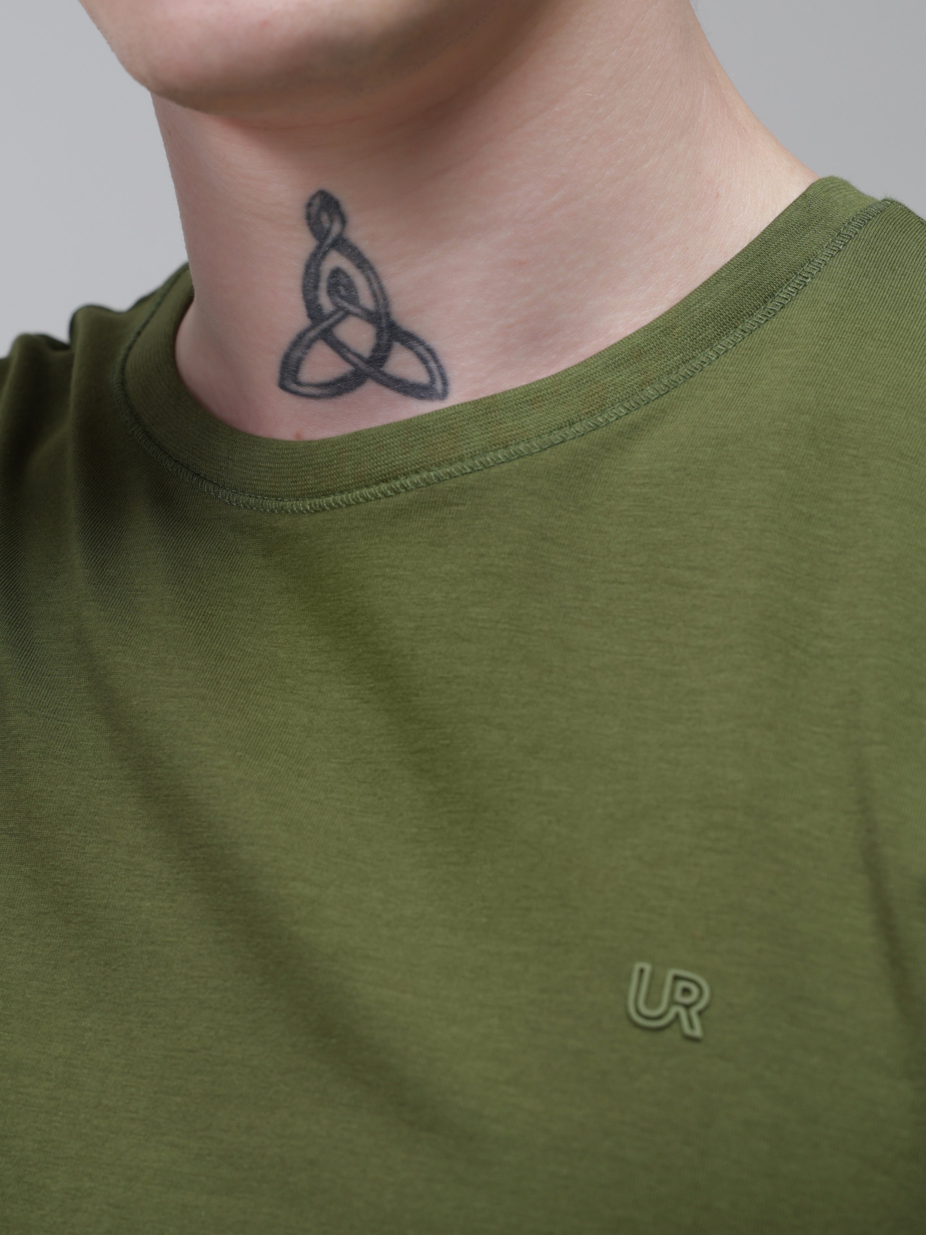 Man wearing green round-neck Turms T-shirt, featuring stain-proof and water-resistant properties, with visible tattoo on neck.