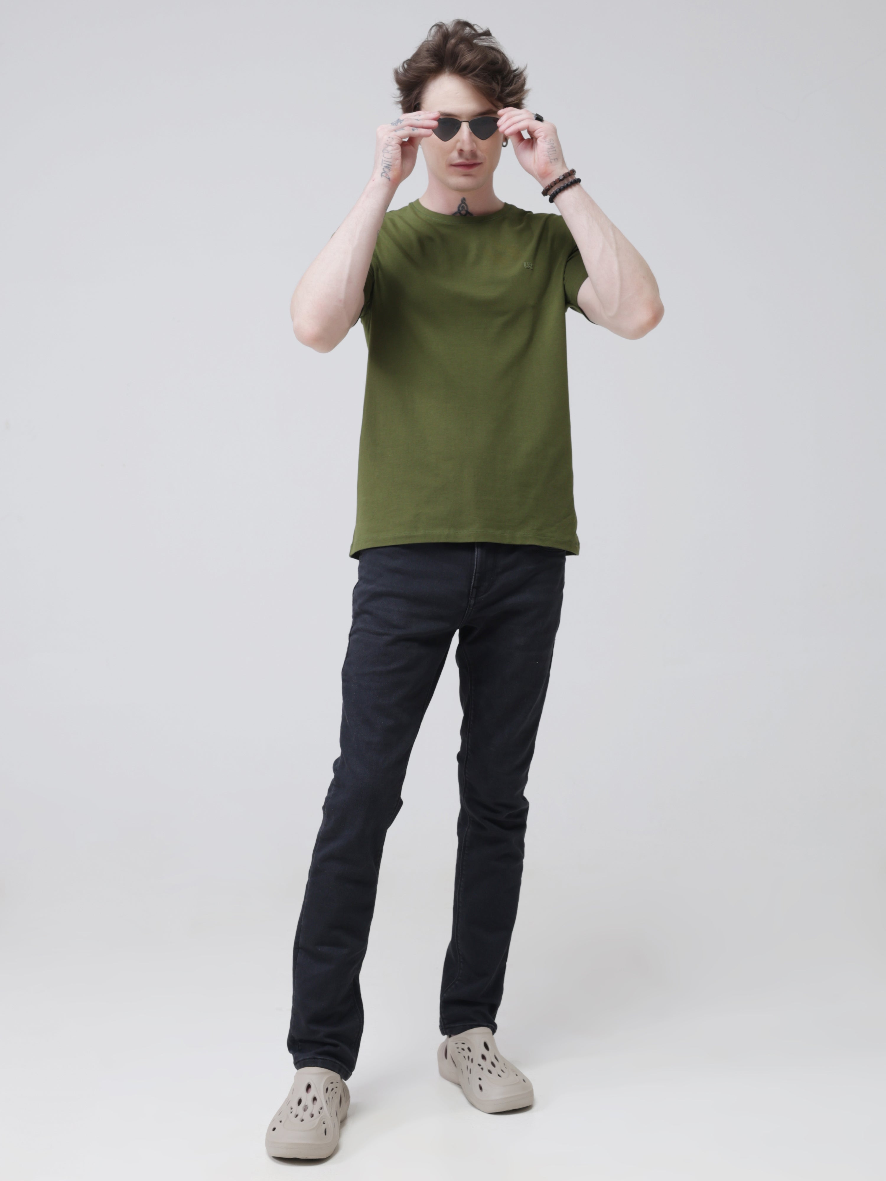 Man wearing a green round-neck Turms T-shirt and dark jeans, showcasing stain-proof, odor-resistant, water-repellent menswear with tailored fit and premium cotton.