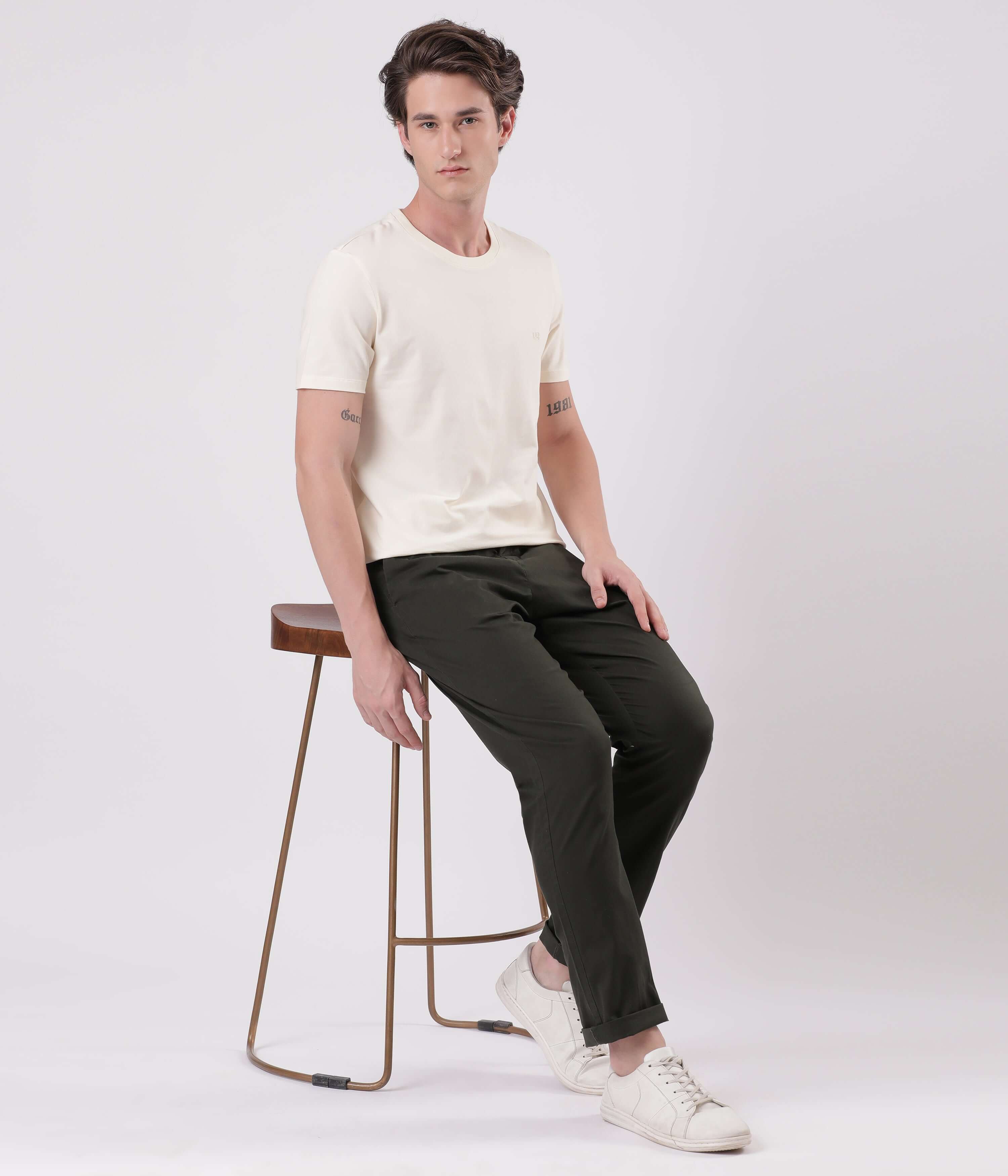 Man sitting on a stool wearing Sage Olive Turms Chino and a light t-shirt, showcasing casual style and comfort.