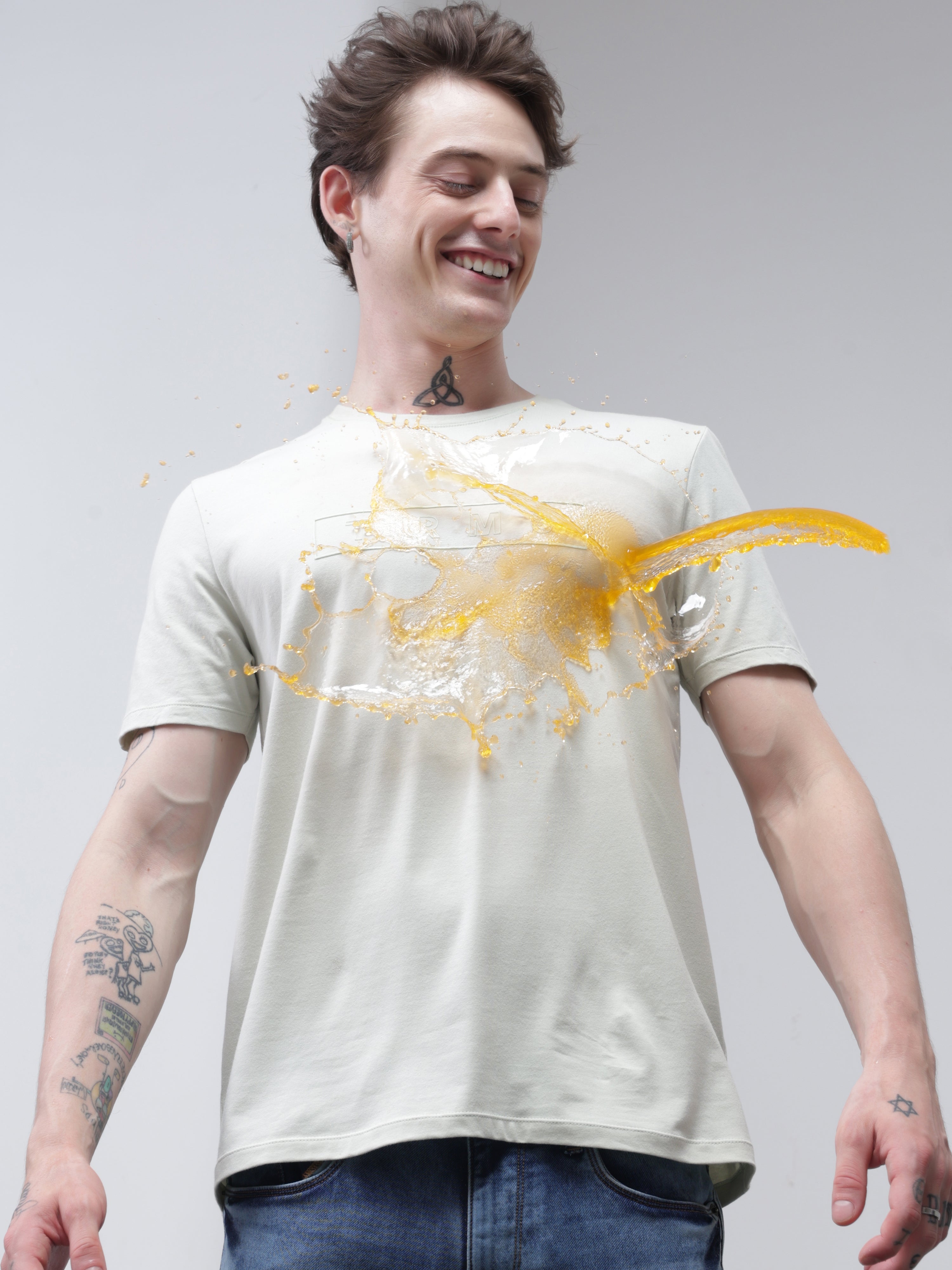 Man smiling as liquid spills onto his stain-proof Turms T-shirt, showcasing its anti-stain, anti-odor, and stretchable properties.