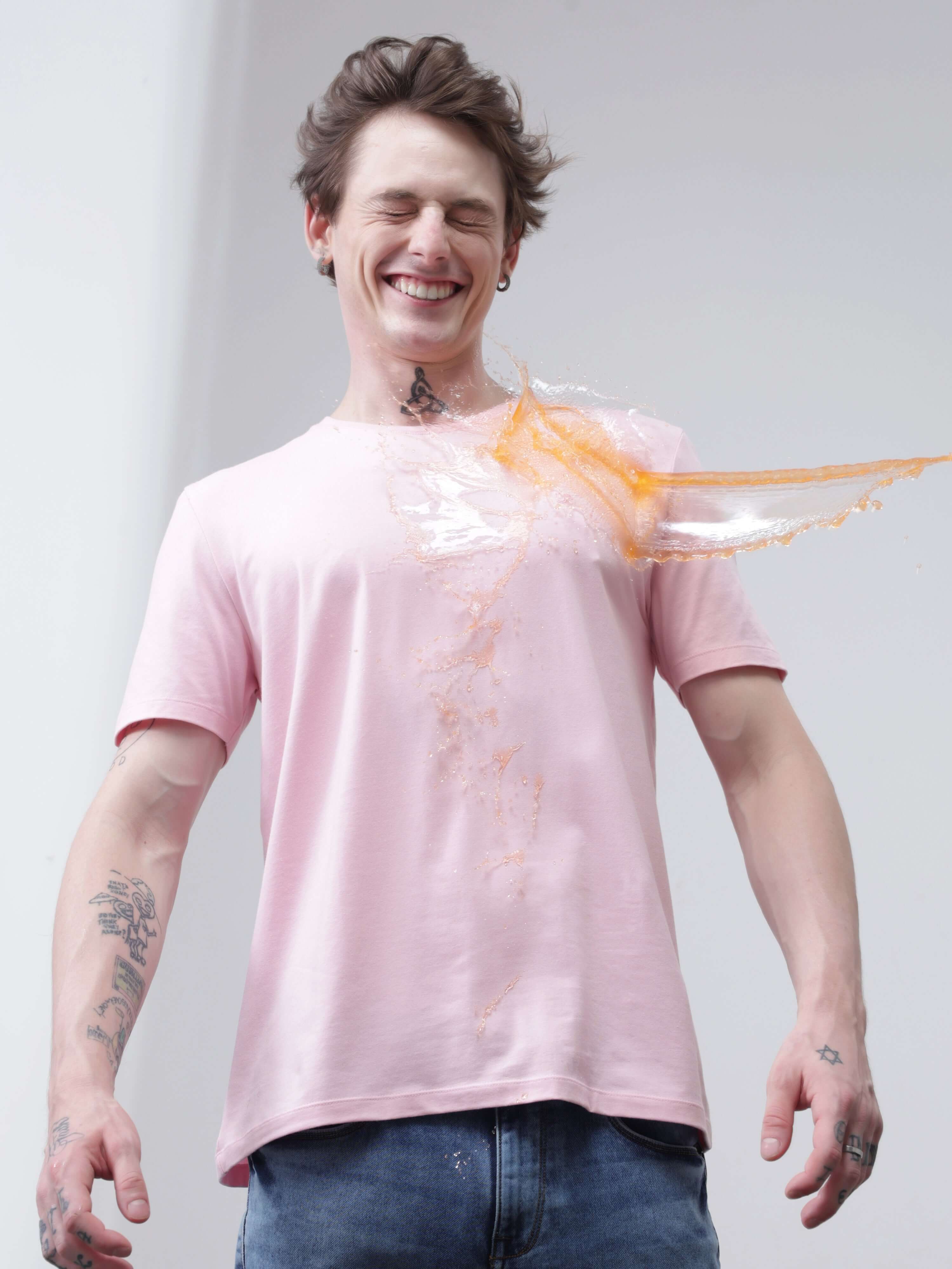 Person smiling while wearing a stain repellent, odor-resistant, stretchable Turms T-shirt as liquid spills but doesn't stain, showcasing anti-stain technology.