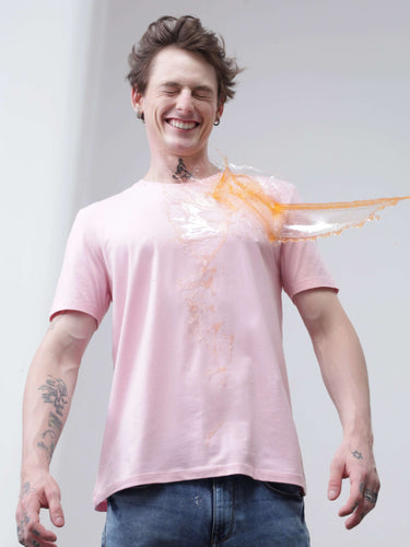 Person smiling while wearing a stain repellent, odor-resistant, stretchable Turms T-shirt as liquid spills but doesn't stain, showcasing anti-stain technology.