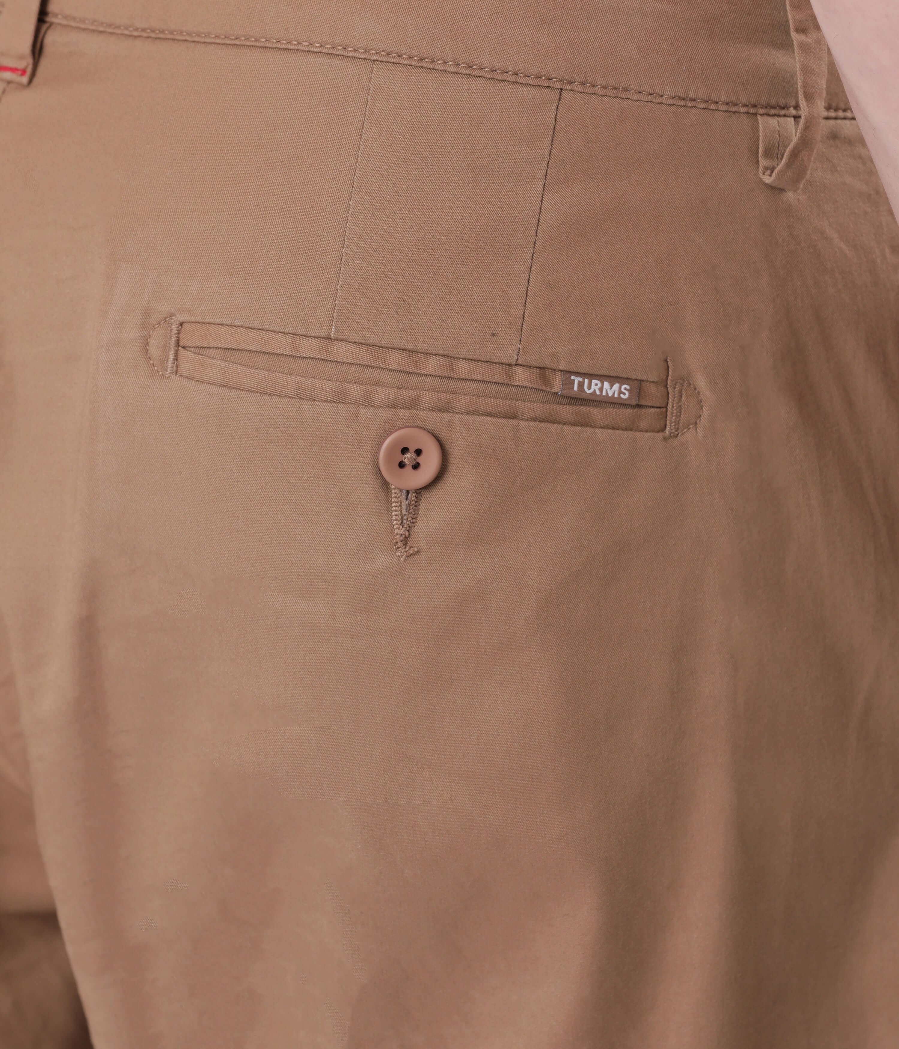 Close-up of a Turms Chino's back pocket showcasing button detail and brand label, highlighting style and quality.