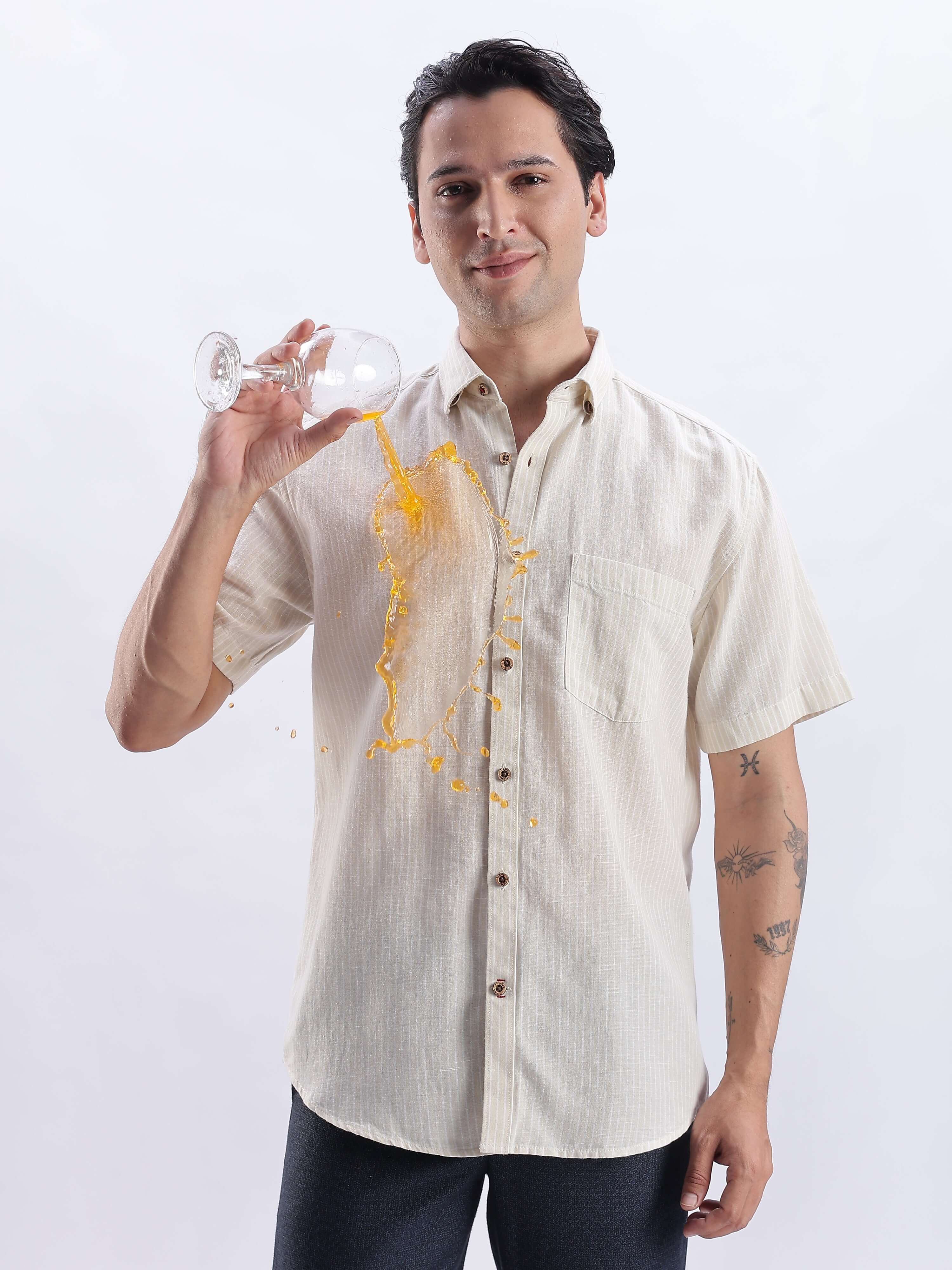 A man in a Sandy Glow linen shirt showcasing its anti-stain feature while spilling juice from a glass.