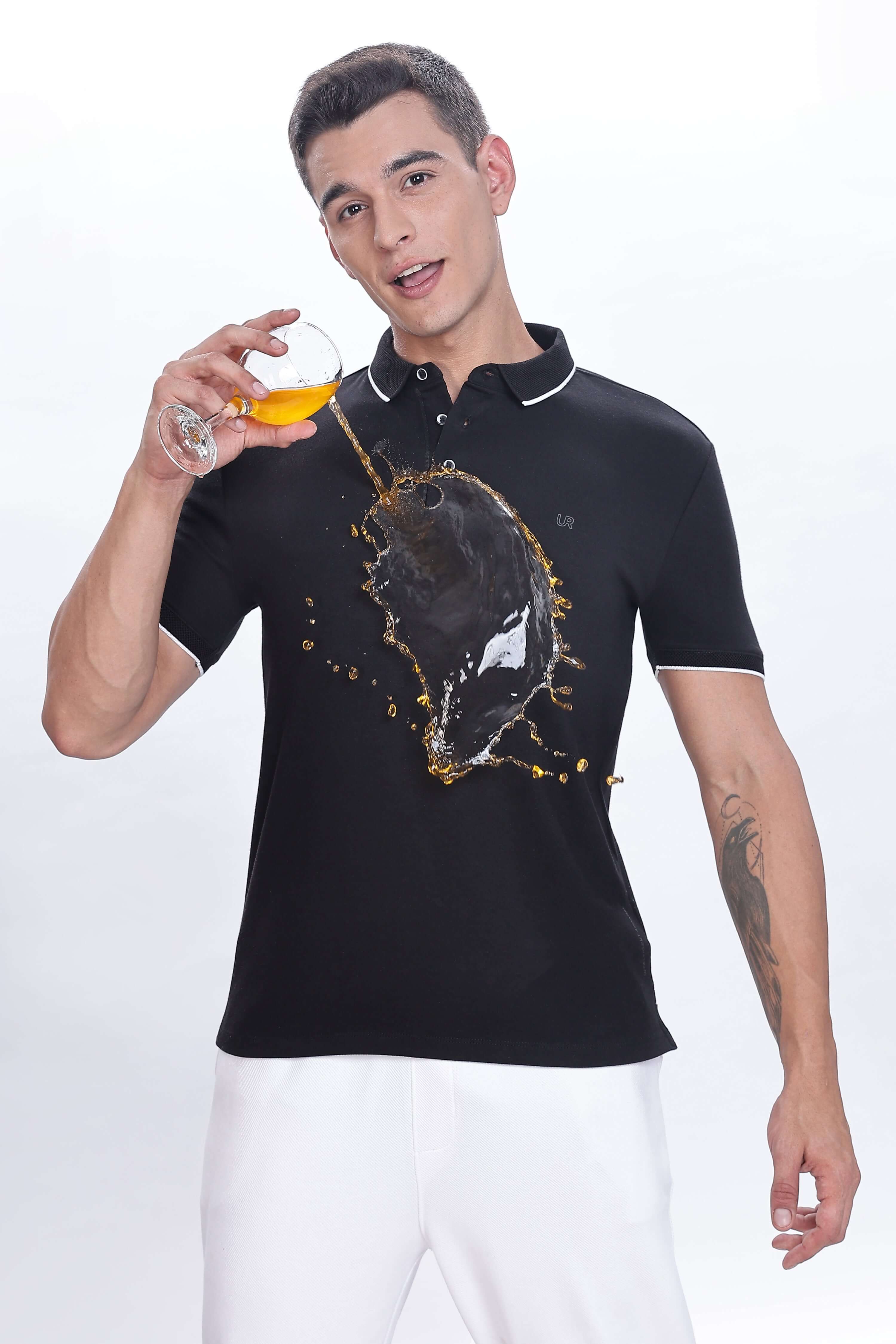 Black Primal black polo tshirt showcasing water proof and anti-stain features while worn by a man holding a drink.