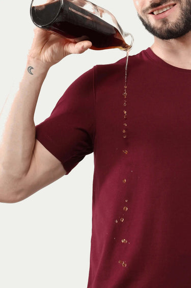 Man wearing cranberry stain-resistant round-neck Turms T-shirt pouring liquid, demonstrating stain-proof fabric in menswear.