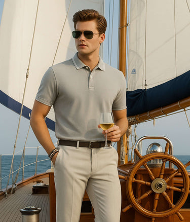 Stylish man wearing Magma Grey cotton polo tshirt on a yacht, enjoying a drink with a scenic ocean backdrop.