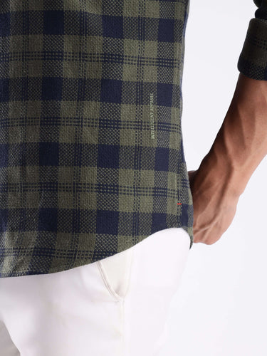 Close-up of a man's hand on the hem of a Turms recycled cotton checked shirt in navy and green.