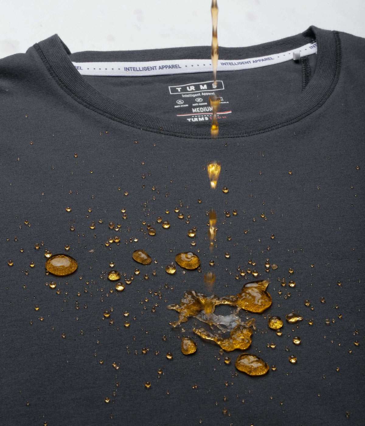 Turms intelligent apparel Charcoal Knight t-shirt showcasing water resistance with droplets on a charcoal grey fabric.