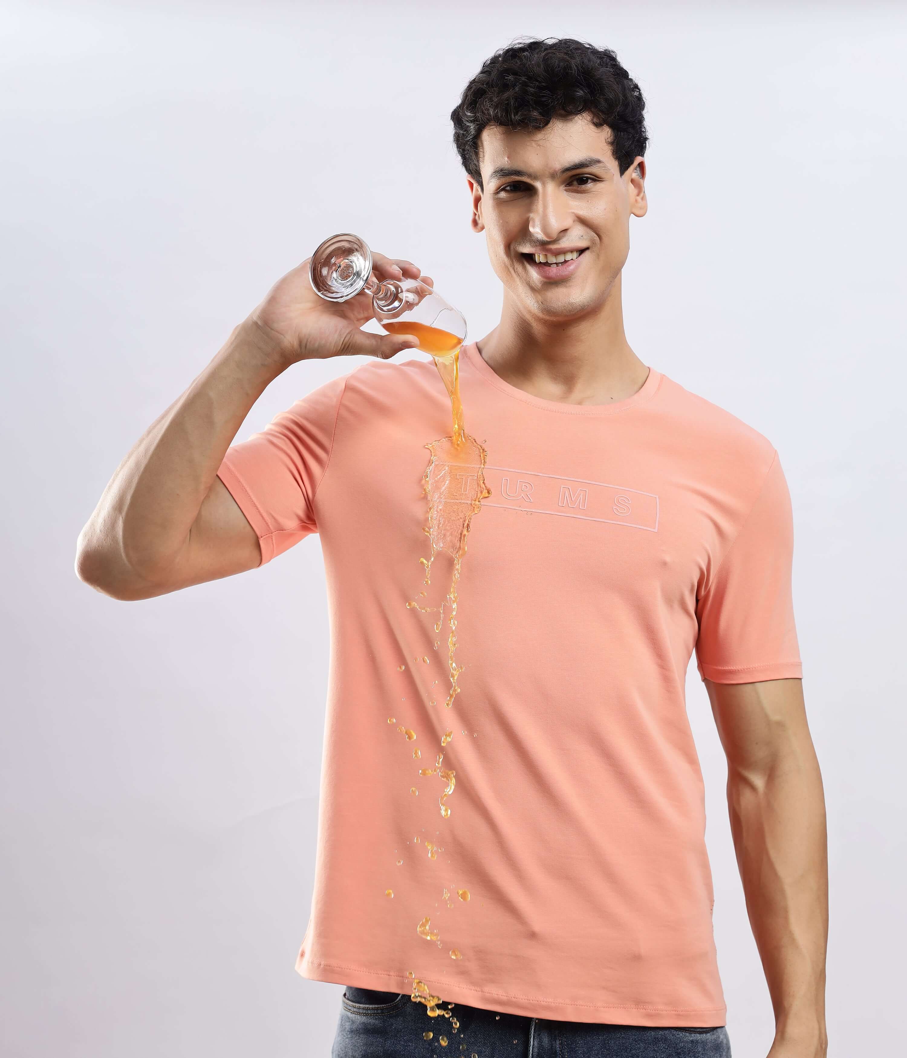 Man wearing Ember Orange cotton tshirt, demonstrating its waterproof and anti-odour features with spilled drink.