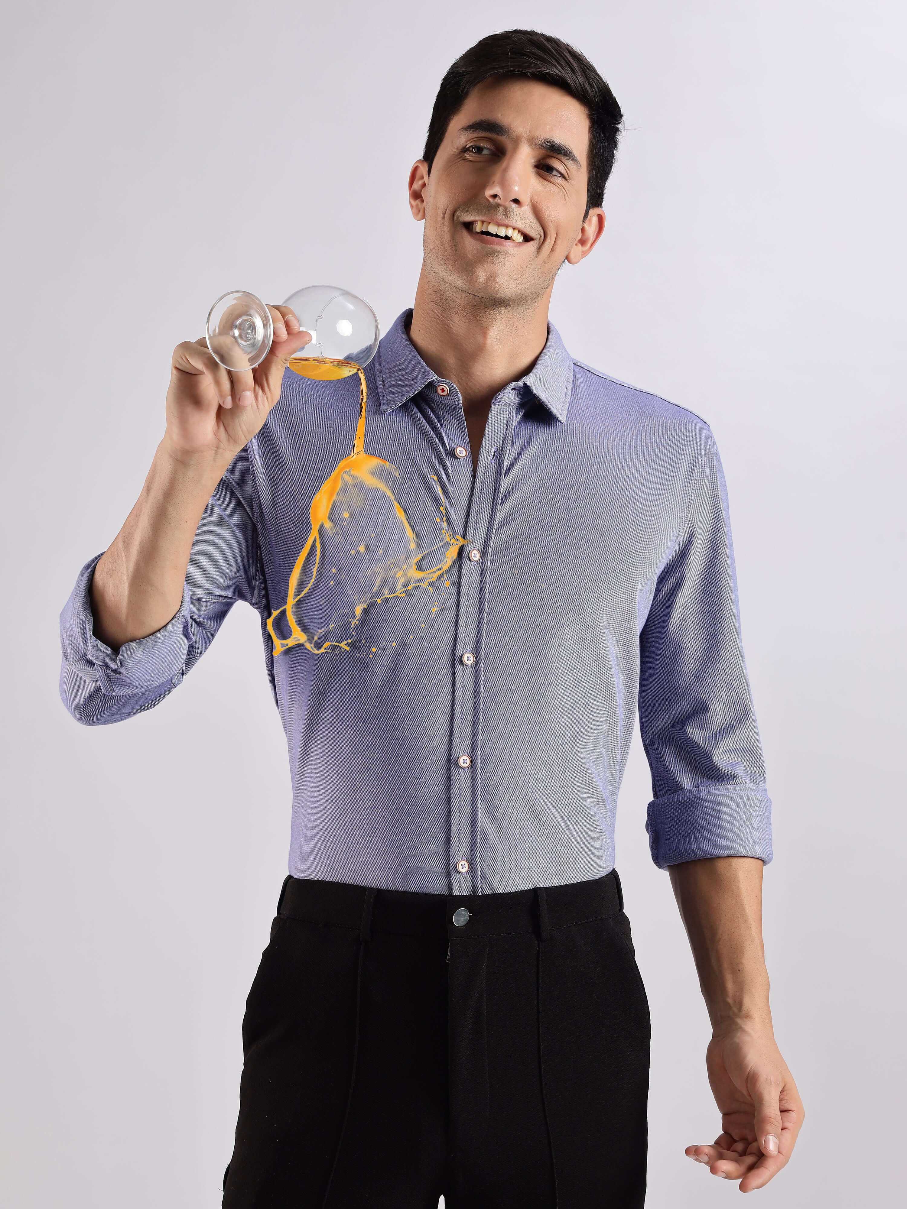 Man wearing a blue knitted shirt, showcasing its anti-stain feature with spilled drink, highlighting premium quality.
