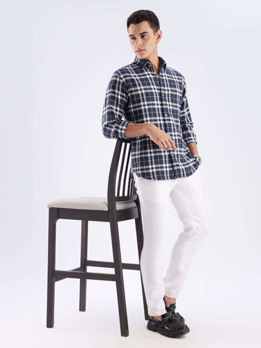 Man wearing Turms recycled cotton checked shirt in navy, paired with white pants, showcasing sustainable fashion.