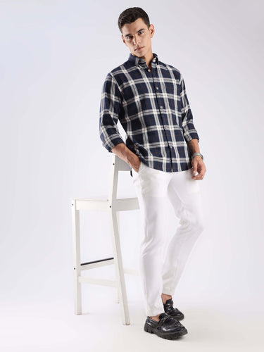 Man in a blue checked recycled cotton shirt with white pants, stylish and sustainable fashion.