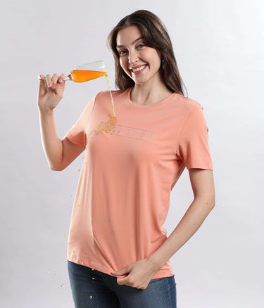 Model wearing Womens casual t-shirt Ember Orange cotton t-shirt demonstrating waterproof feature while pouring liquid from a glass.