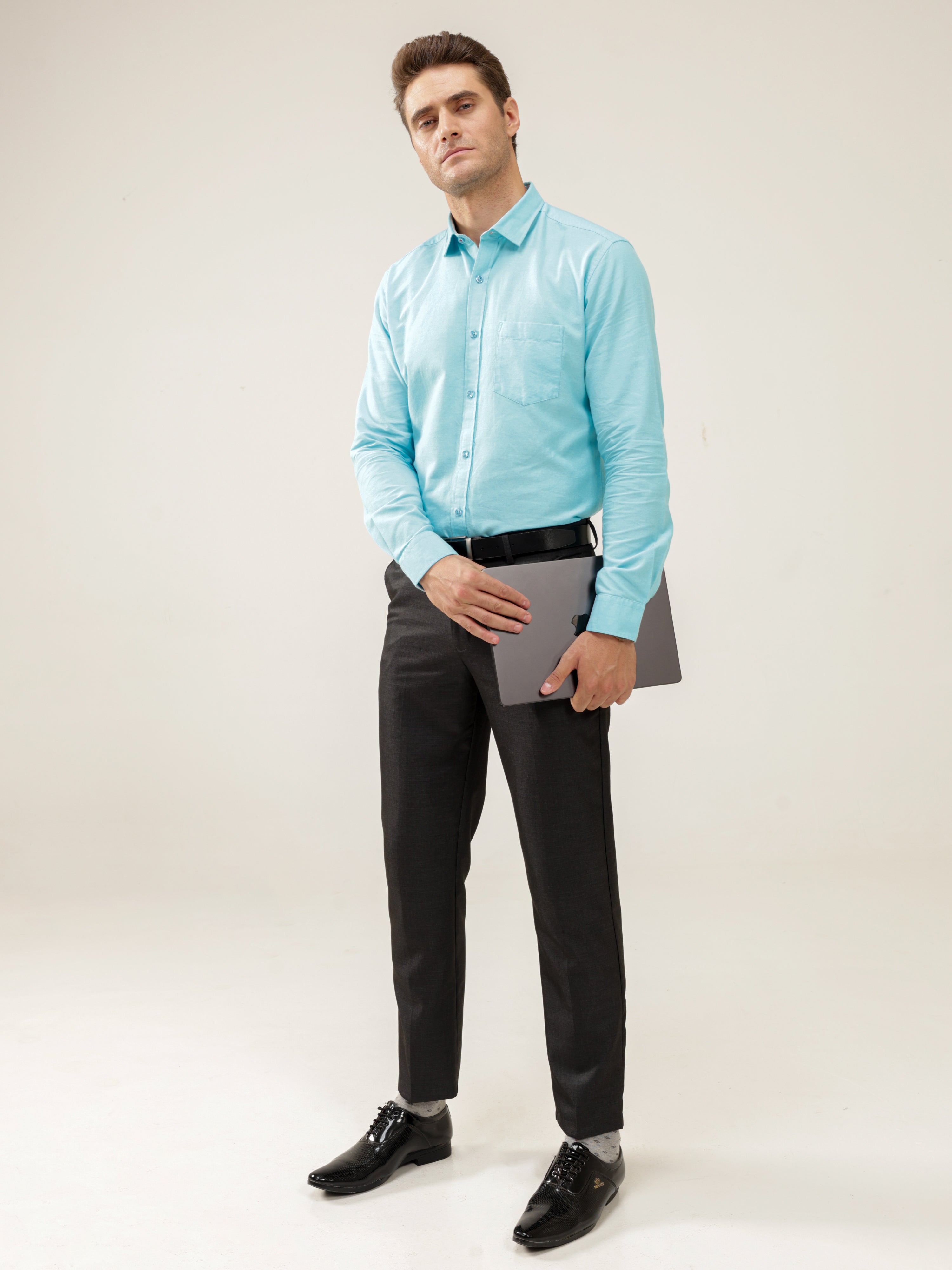 Man wearing a Turquoise Oasis Oxford Turms shirt paired with black trousers, holding a laptop; stylish, anti-stain, water-resistant casual office wear.