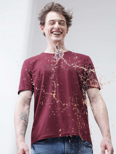 Man wearing Burgundy Elite Turms T-shirt demonstrating anti-stain and anti-odor properties as liquid spills but doesn't soak.