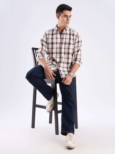 Man wearing a stylish recycled cotton checked shirt, seated on a bar stool, showcasing sustainable fashion.