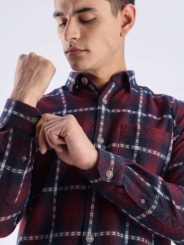 Man adjusting cuff of a stylish checkered recycled cotton shirt, showcasing sustainable fashion by Turms.