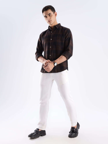 Man wearing a rustic recycled cotton checked shirt with white pants and black shoes, showcasing sustainable style.